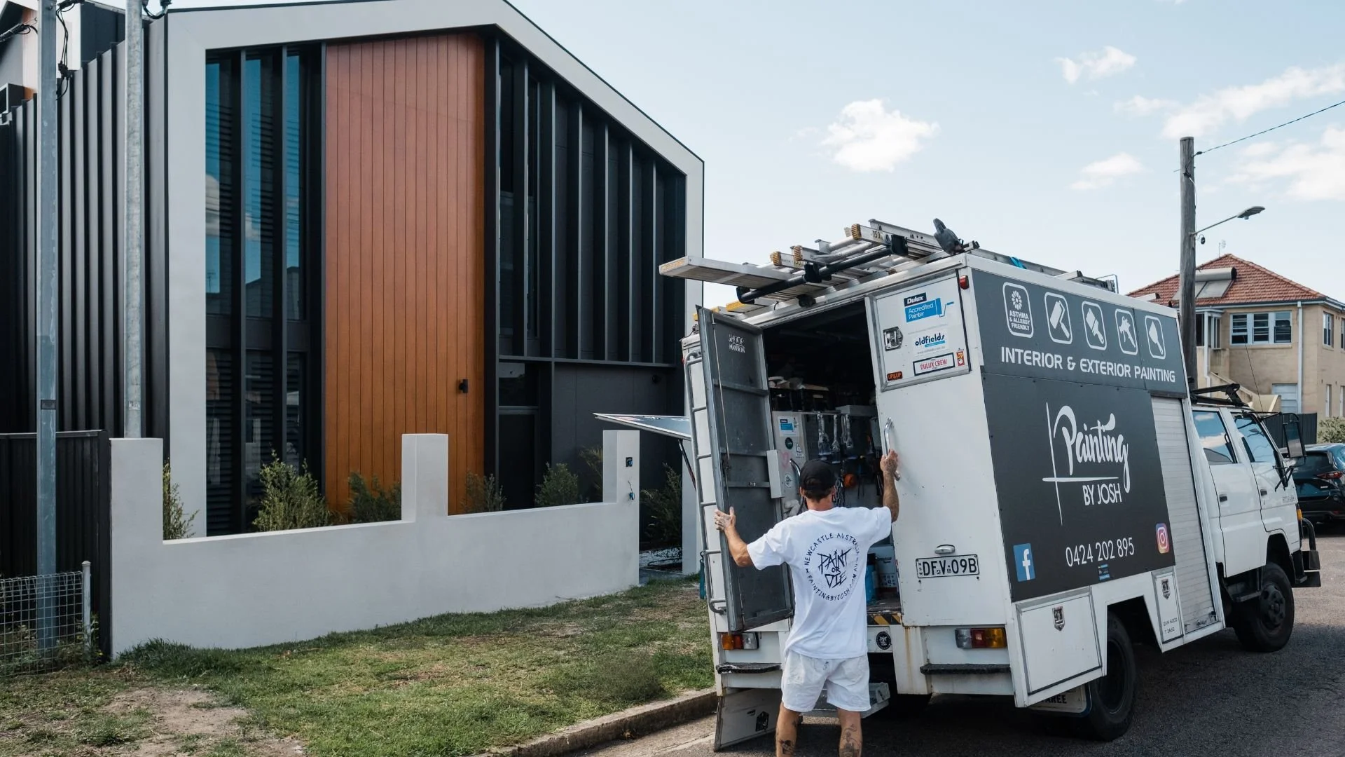 Person unloading equipment from a painting company's truck near a modern building exterior.