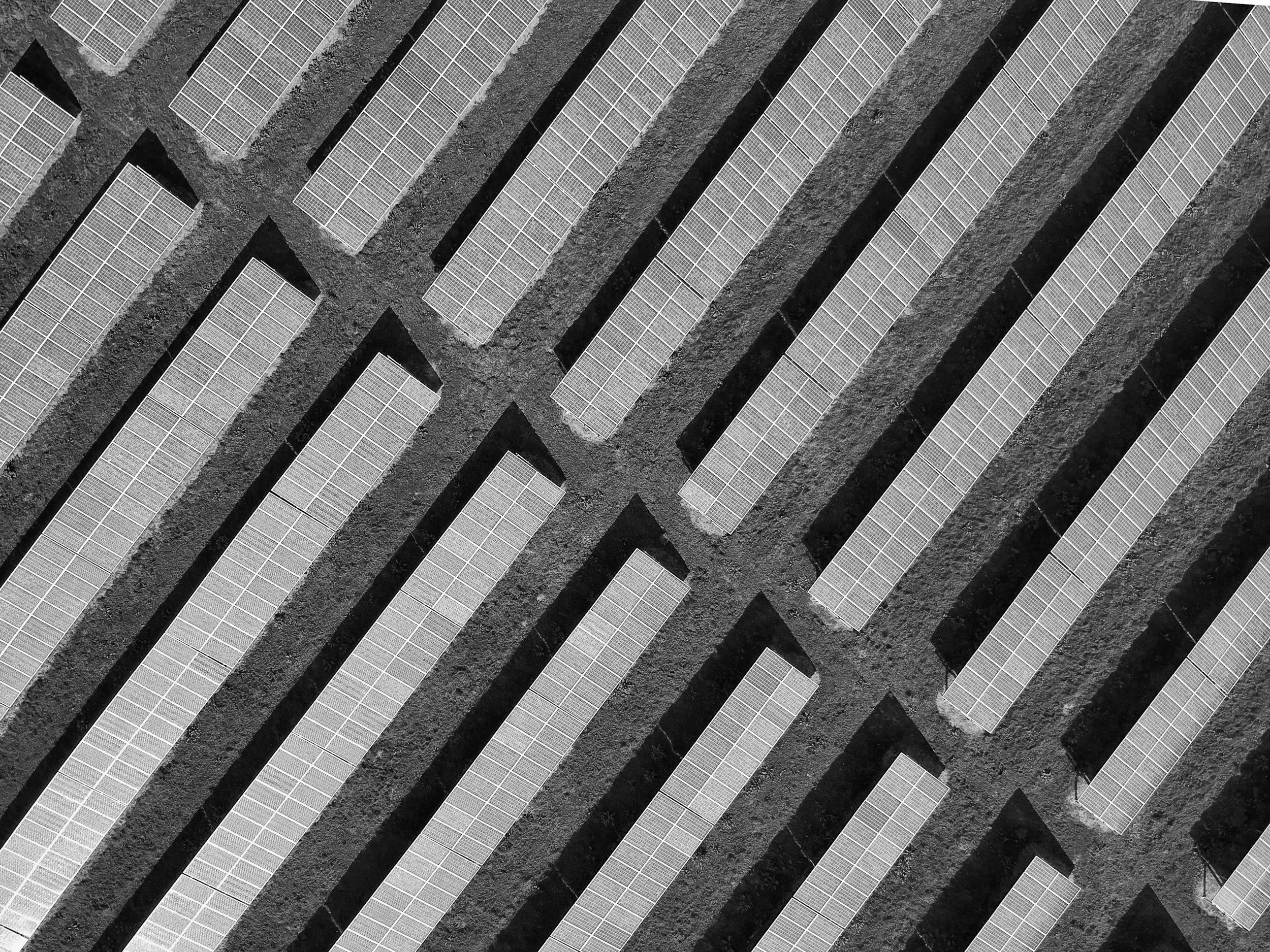 An aerial view of solar panel installations arranged in parallel rows on a gravel surface.