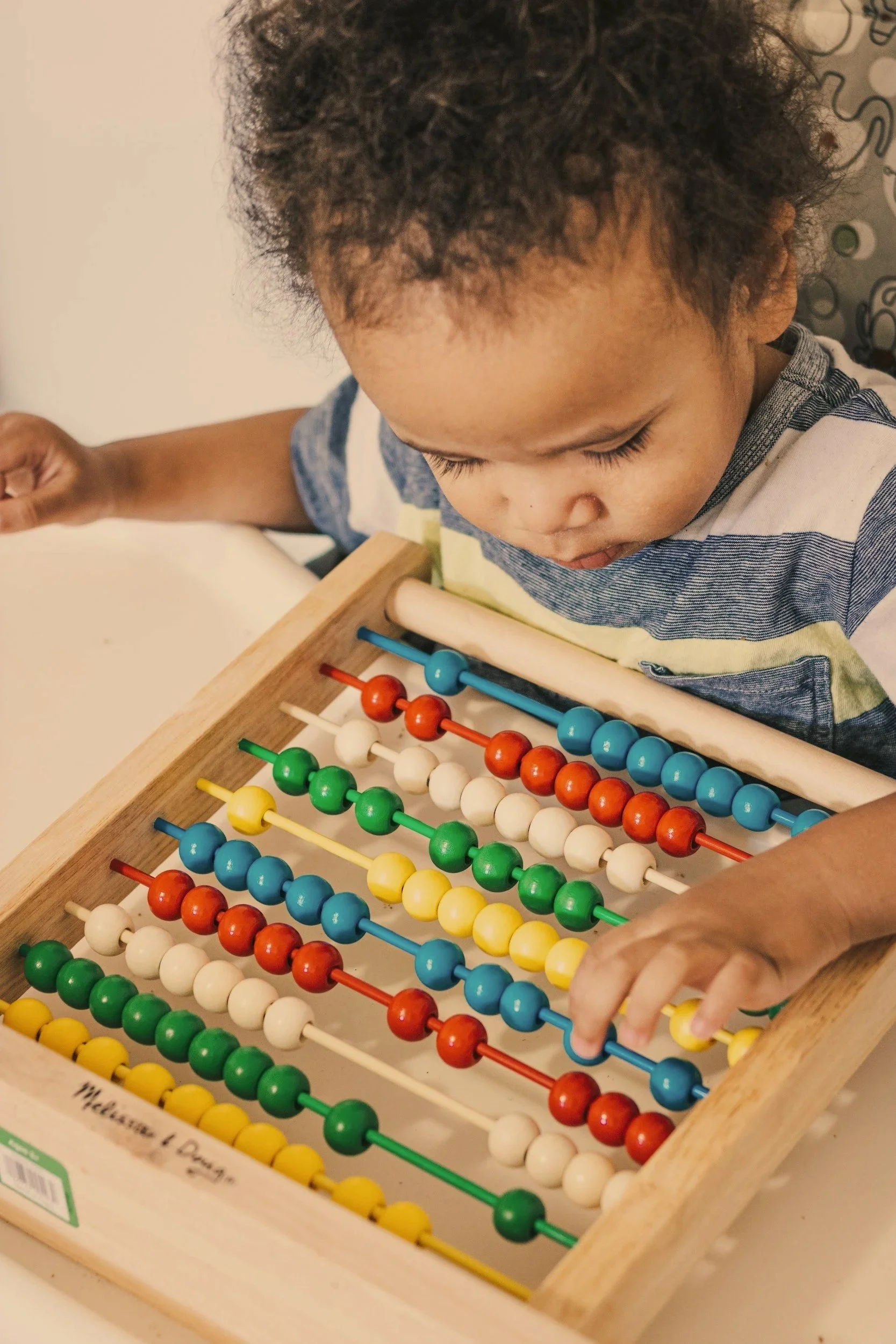 A young child with light brown hair, wearing a bright yellow shirt, holding a colorful toy camera with a smiley face on it, focusing on the toy.