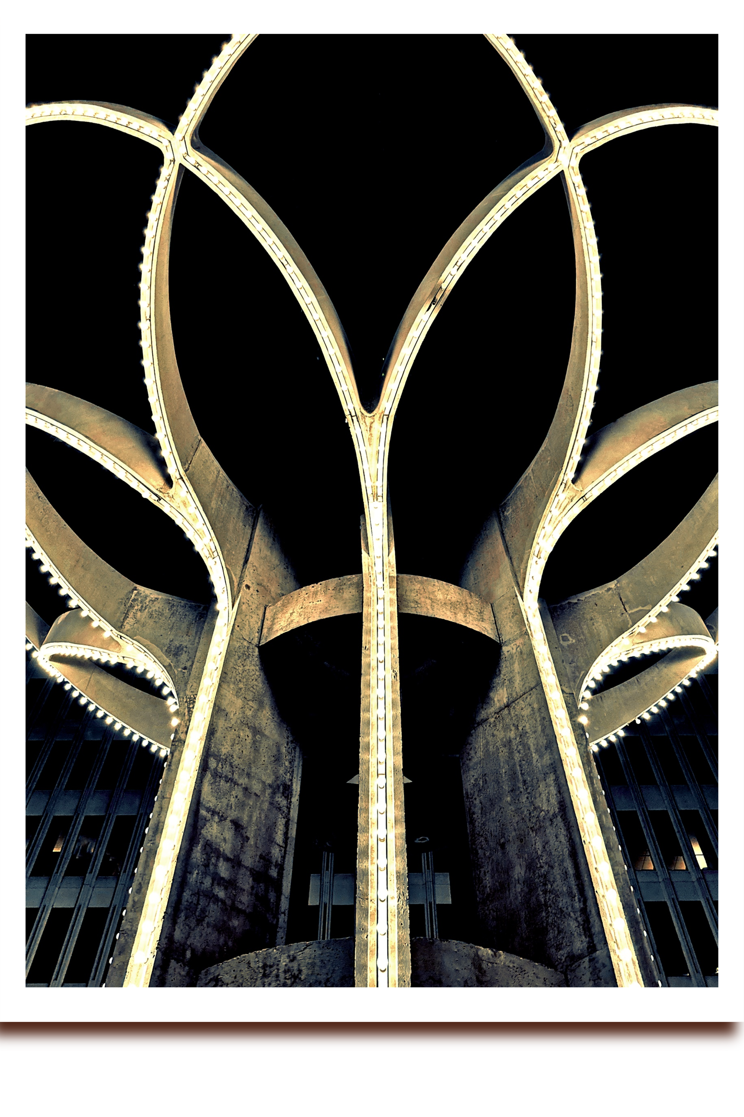 Art Deco tower at night under heavy clouds, illuminated architectural details emerging from darkness, urban modernist structure photographed after hours.