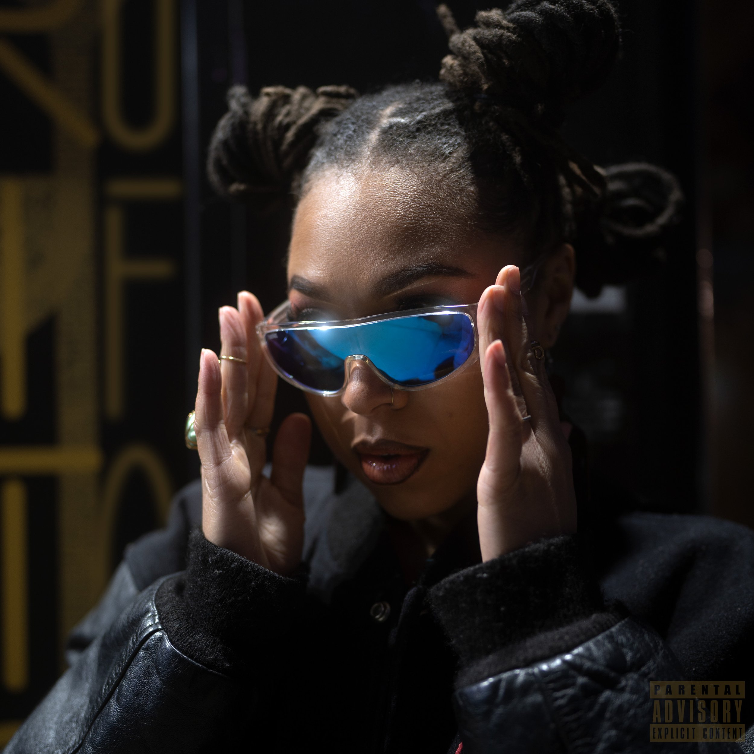 A woman with dreadlocks wearing reflective blue sunglasses, holding them with both hands, dressed in a black leather jacket, in a dark setting. Oliv Blu cover art for single UFO (Demo).