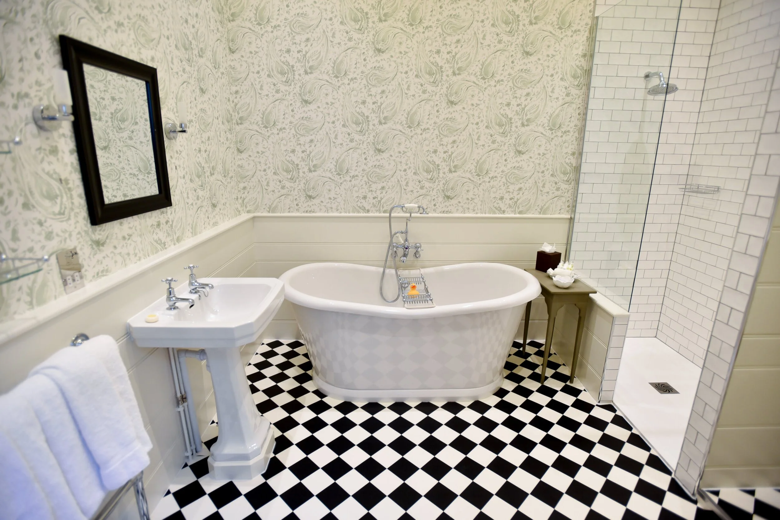 Bathroom with vintage clawfoot bathtub, walk-in shower, wooden accents, window with patterned curtain, hardwood flooring, and mix of modern and antique fixtures.