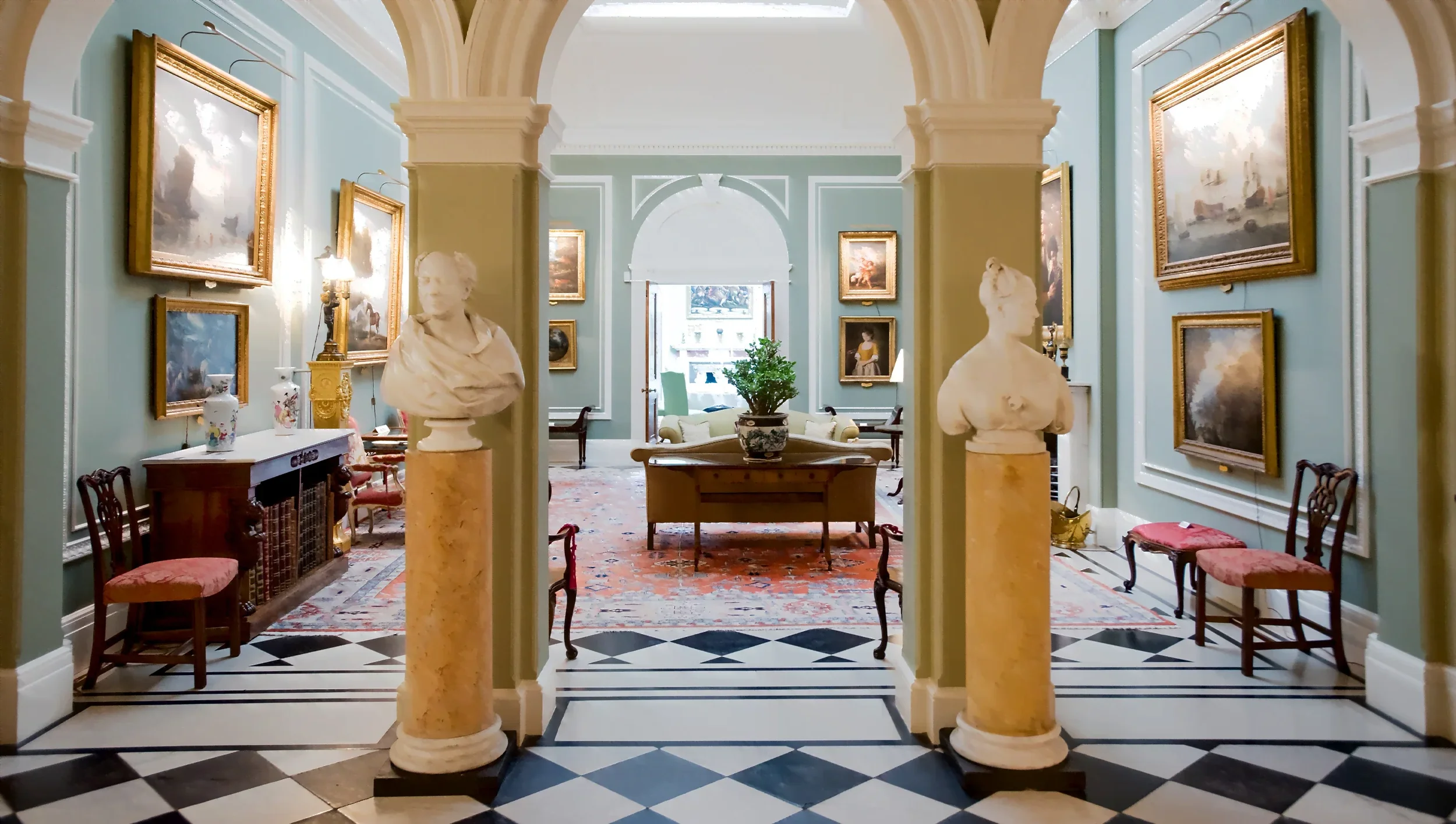 A cozy room decorated with antler chandeliers, ornate wallpaper, vintage furniture, and mannequins with elaborate headpieces.