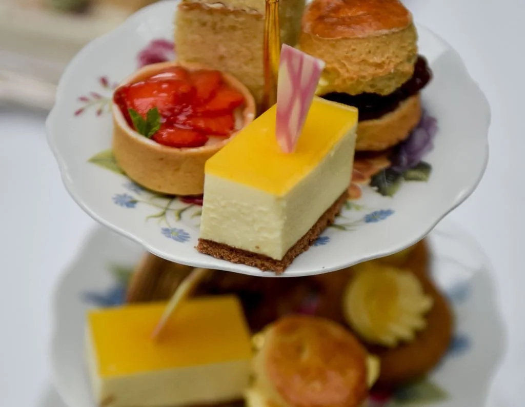 Hand pouring tea over a bowl of ramen with vegetables, on a dark wooden table.