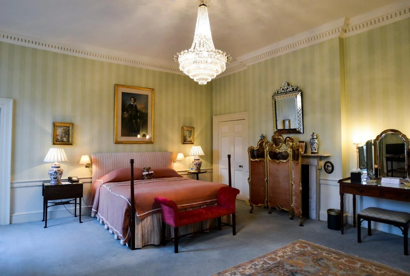 A vintage-style bathroom with a clawfoot tub surrounded by lit candles, a small sink, a mirror, framed pictures on the wall, and natural light coming through a window.
