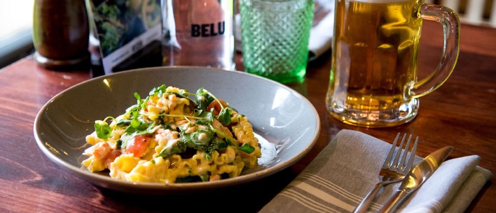Assorted canapés and glasses of red cocktail on a black slate serving board, garnished with microgreens, on a dark red velvet tablecloth.