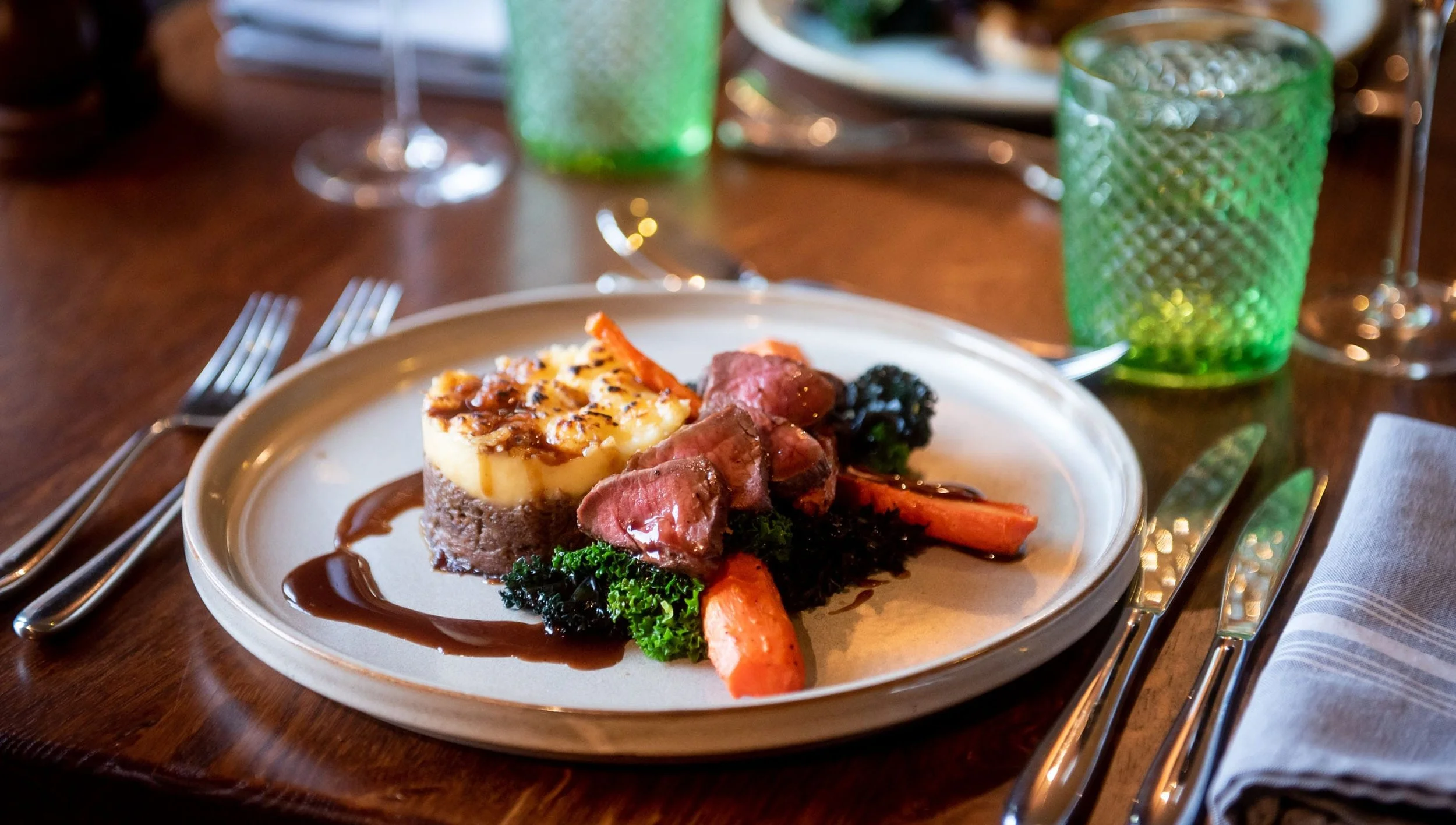 Vegetable spring rolls filled with assorted colorful vegetables on a wooden surface, with a hand slicing more vegetables in the background.