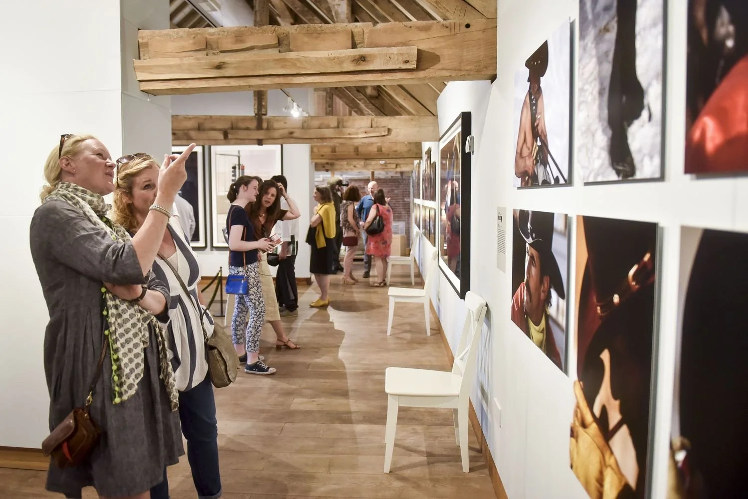 Elegant living room with ornate ceiling, large window with pink curtains, a fireplace with a fire, and various colorful vintage armchairs and sofas, decorated with flowers and artwork.