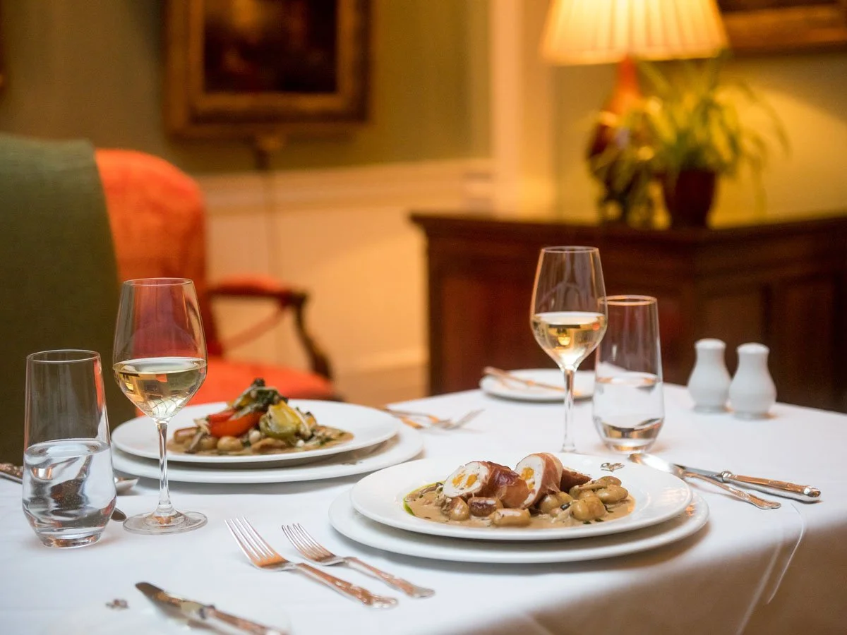 A chocolate cake with a glossy chocolate glaze, topped with pomegranate seeds and sliced almonds, with a slice taken out revealing layers of frosting and cake, surrounded by piped cream or frosting around the base.