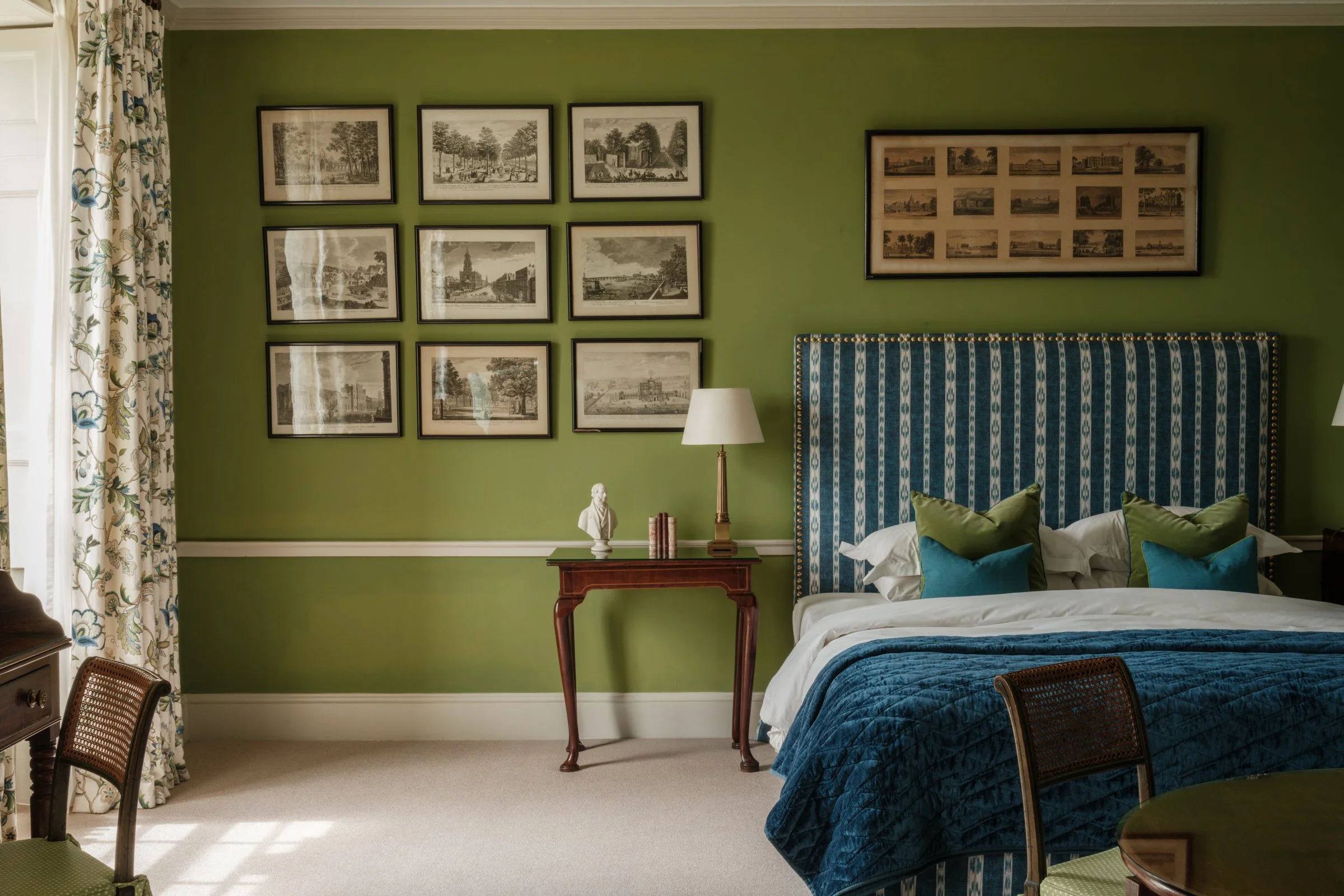 Bathroom with a vintage clawfoot bathtub, a window above it, framed artwork on white walls, a mirrored vanity with sconces, a toilet with a wooden seat, and a small sink with a towel and toiletries.