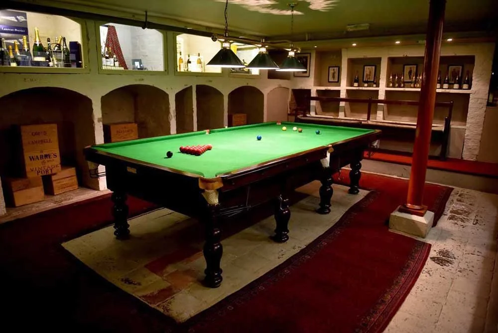Elegant room with a wooden table, a vintage clock, a coral-colored sofa, green potted plants, and a large portrait of a woman in a dress paintings on the wall.
