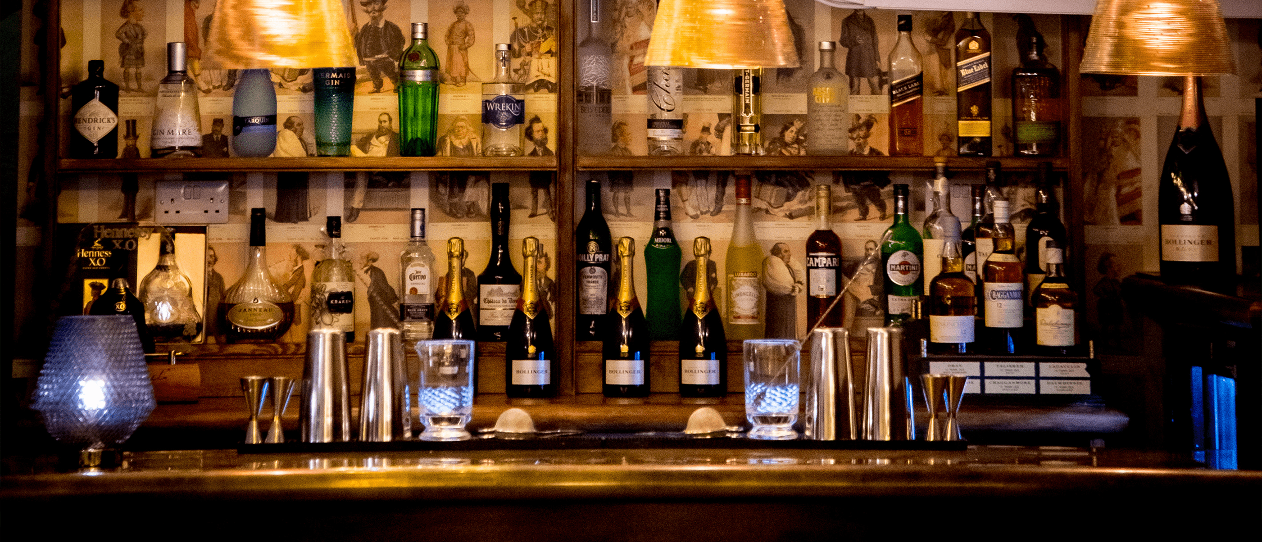 Interior of a cozy bar with dark wooden furnishings, black velvet chairs, a chandelier, and a large window in the background.