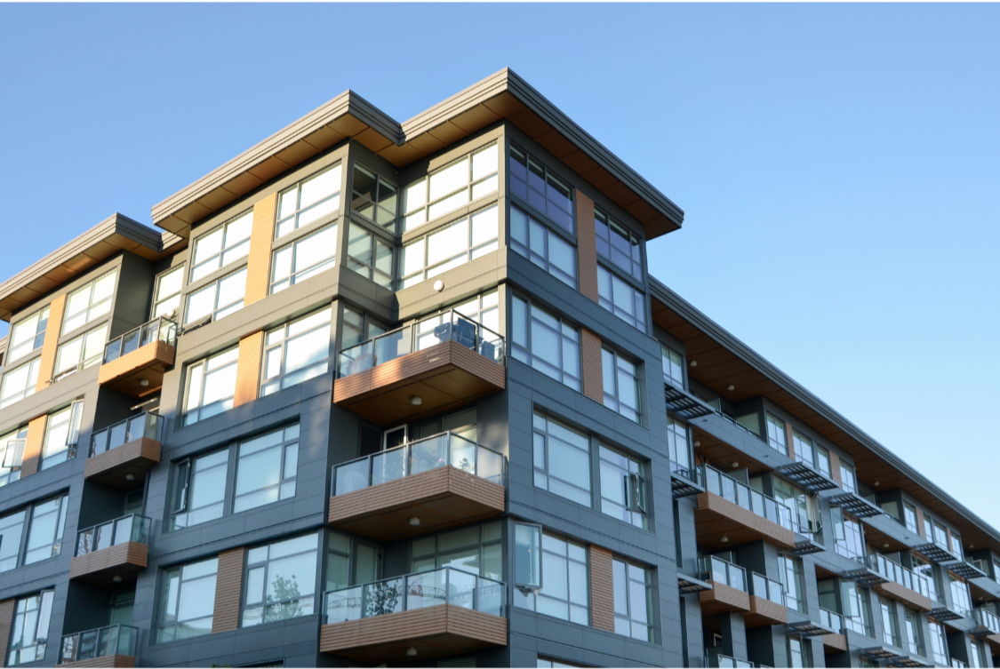 Modern multi-story apartment building with glass balconies and large windows, under a clear blue sky.