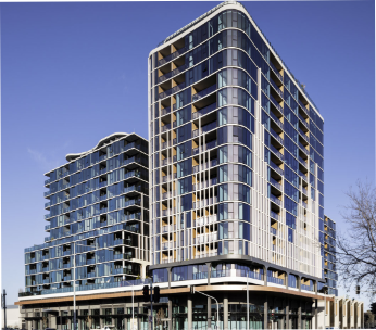 Modern high-rise apartment buildings with glass facades and rounded edges against a clear blue sky.