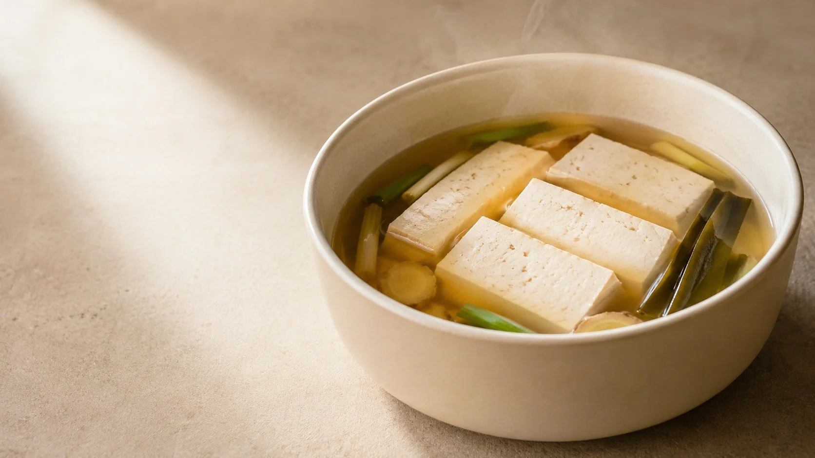 Firm tofu resting in a gently simmered aromatic broth to infuse flavour before serving.
