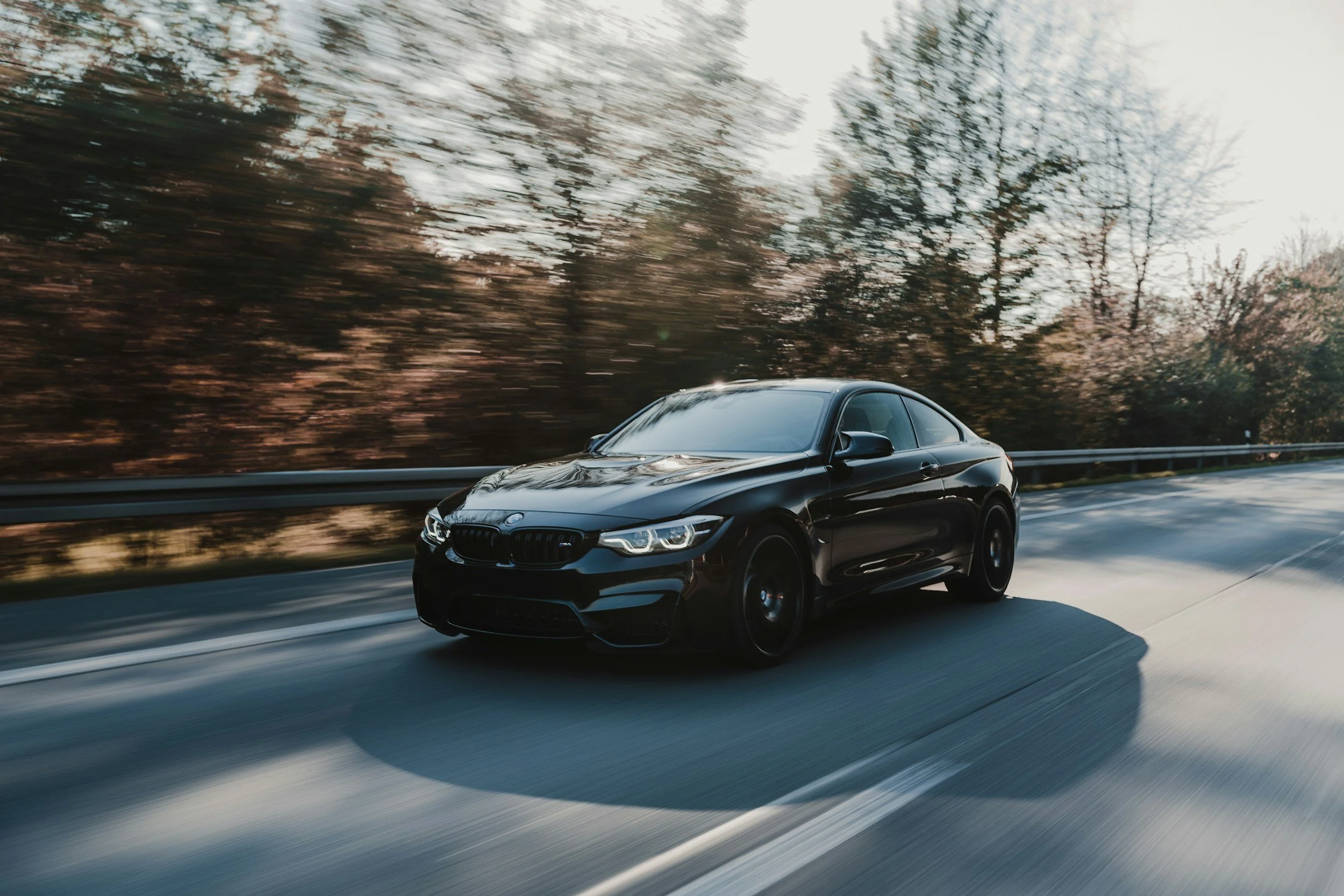 Black sports car driving on a highway with blurred trees in the background.