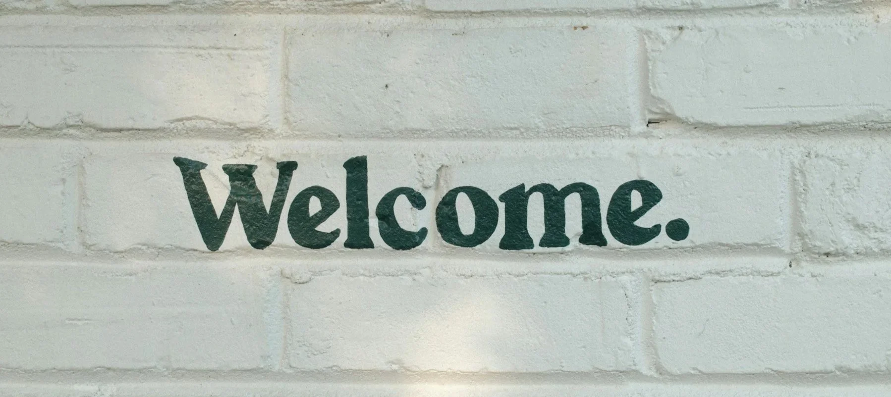 Green text that says "Welcome" painted on a white brick wall.