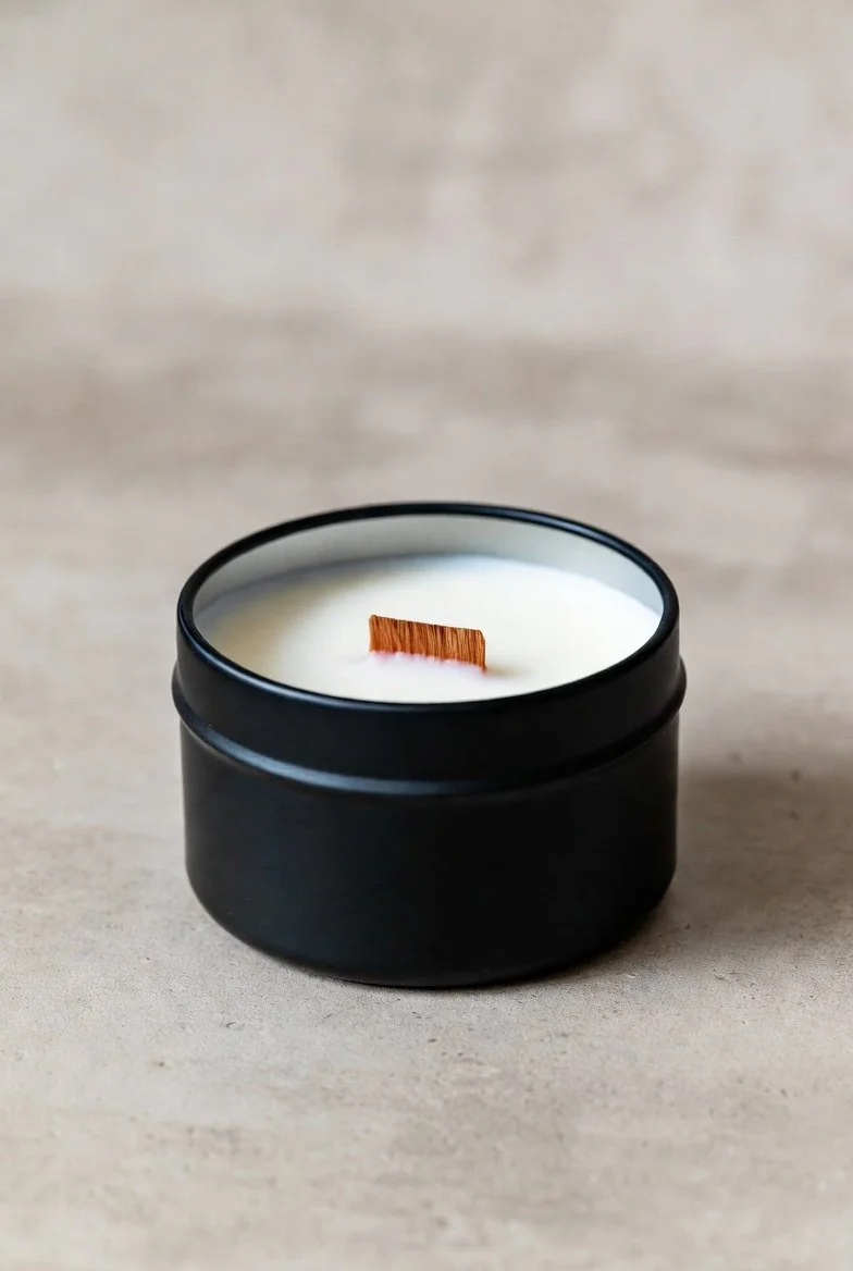 A black candle jar with a wooden wick, filled with white wax, on a light-colored surface.
