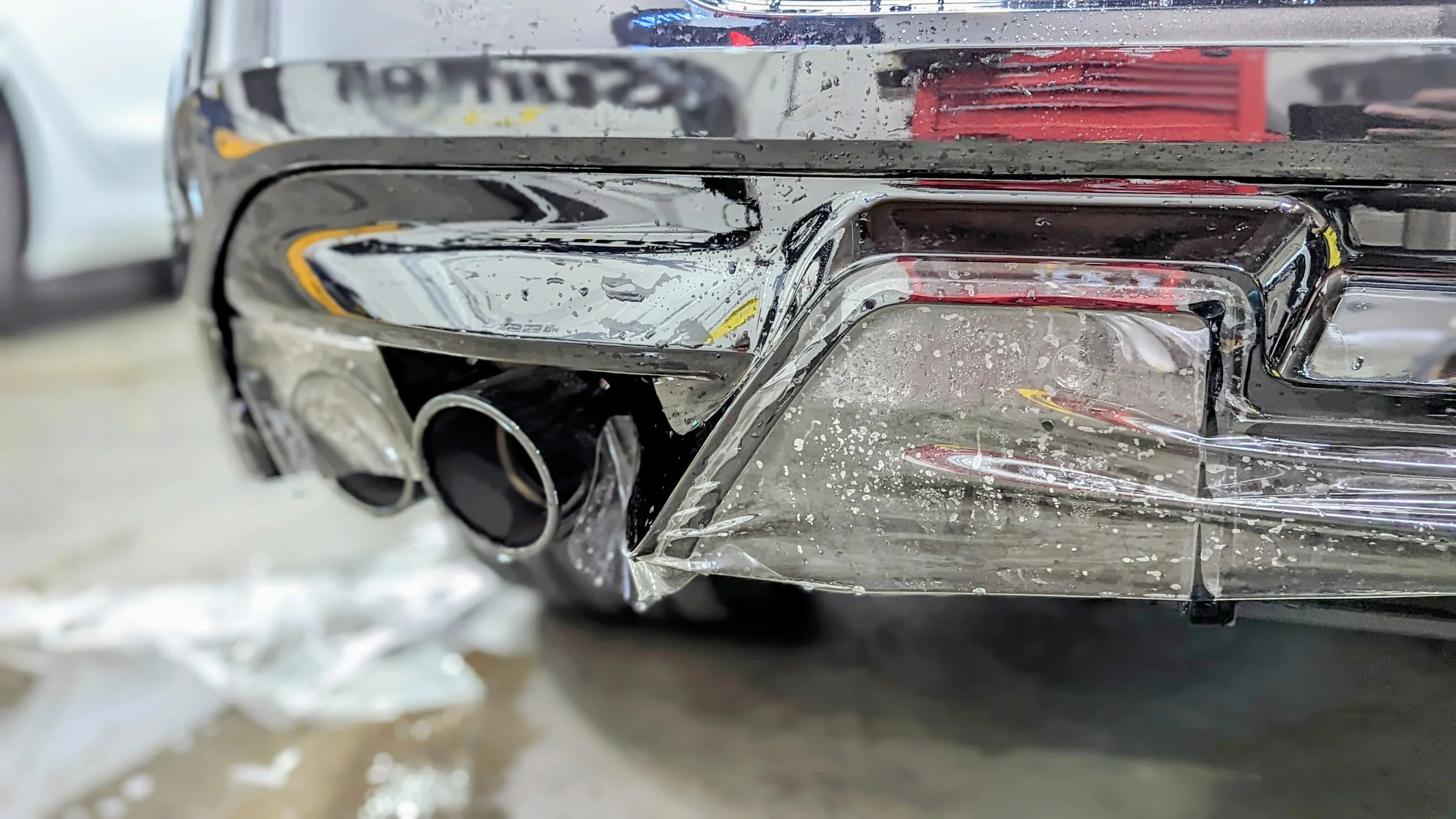 Close-up of a chrome car bumper with water spots and a black exhaust pipe.