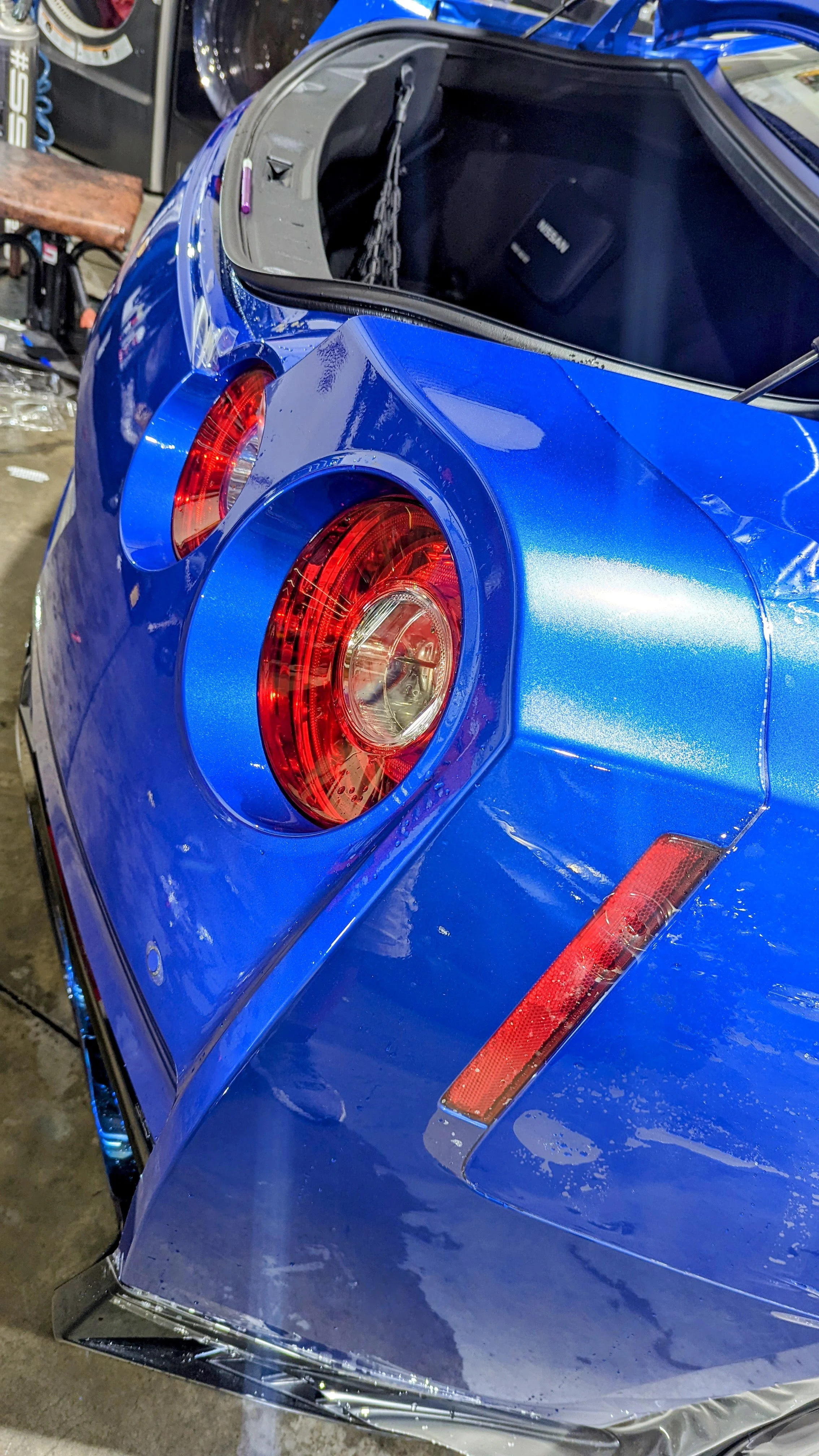 Close-up of the rear end of a shiny blue sports car, showing the circular red tail lights and part of the trunk.