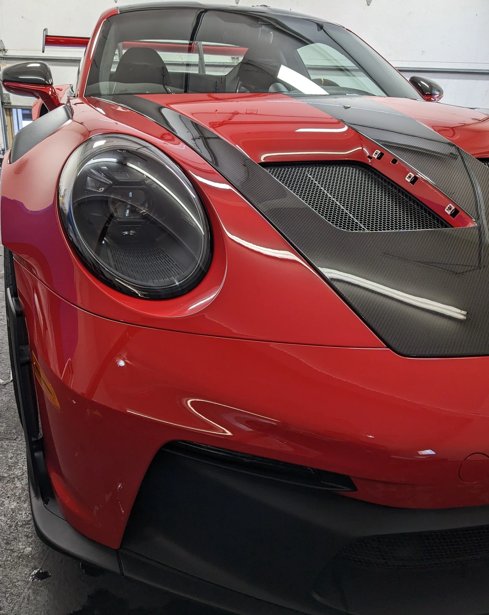 Close-up of the front of a red sports car with a black carbon fiber hood and aerodynamic design.