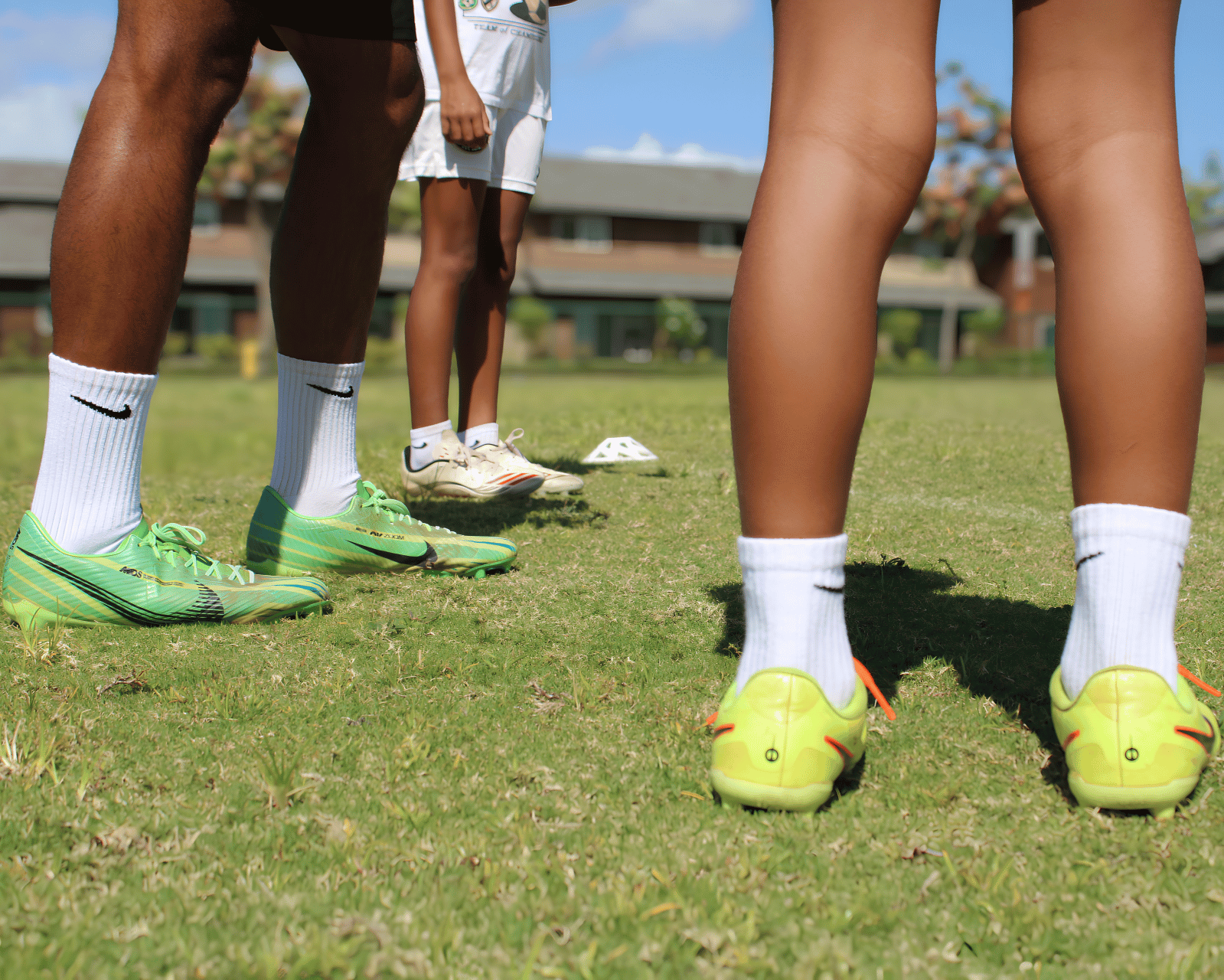Close-up of children's legs and feet on a grassy field, wearing sports shoes and socks, with a focus on their athletic stance.
