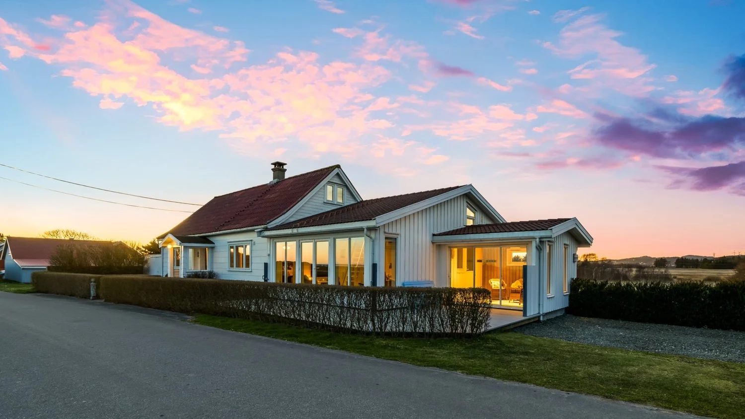 Hvitt hus med opplyste vinduer i solnedgang, fotografert av Bolio