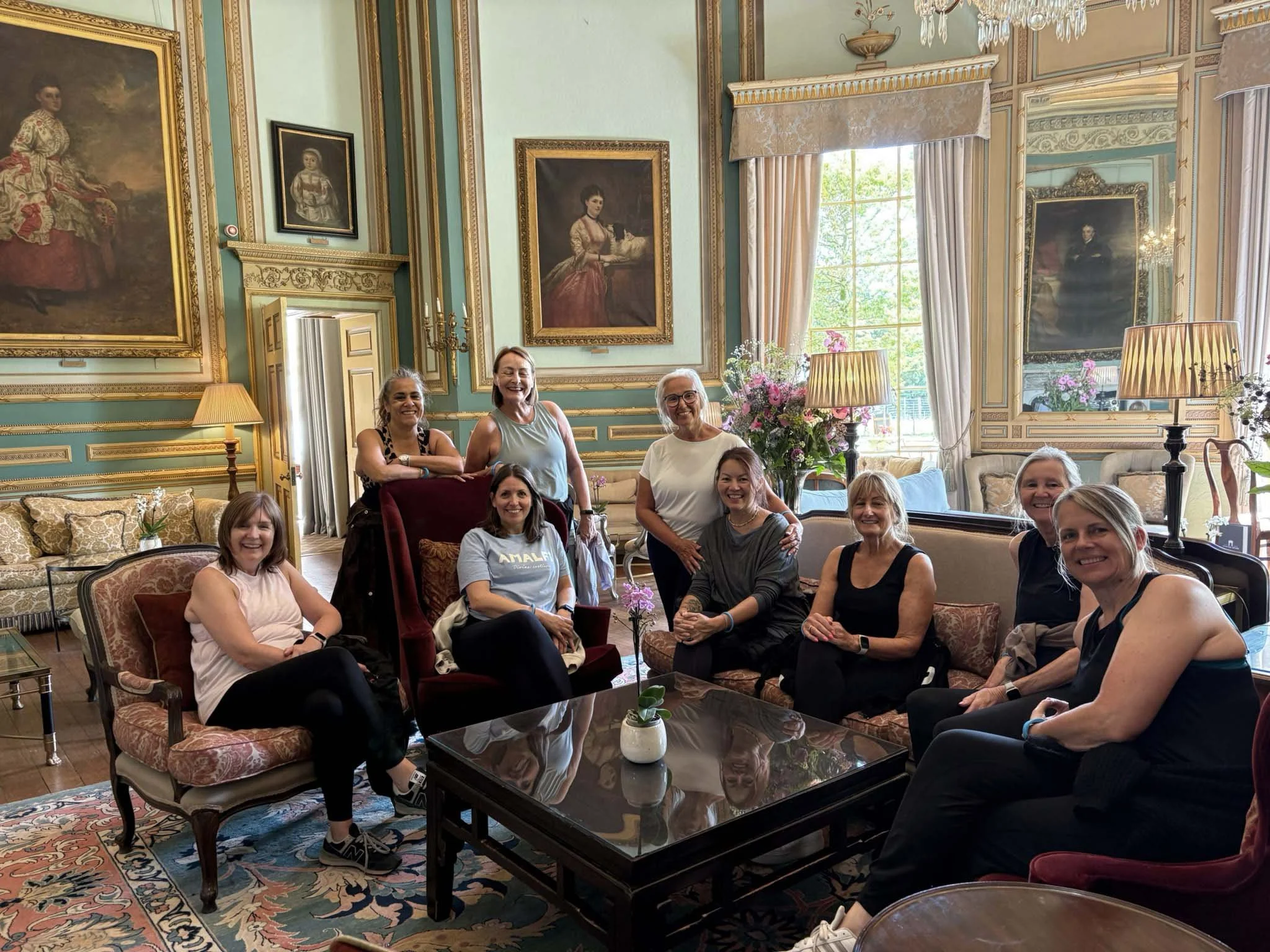 Group of people smiling and posing for a photo in a decorated room with large paintings and chandeliers.