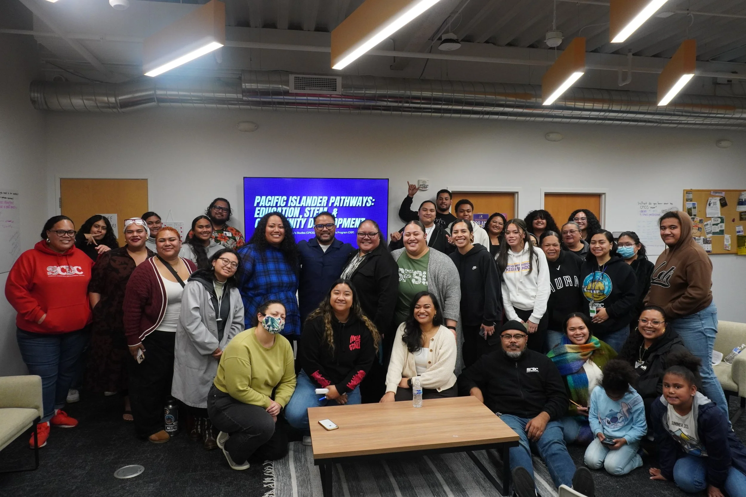 Group photo of diverse people in a room with a digital screen that reads 'Pacific Islander Pathways: Education, STEM & Community Development.'