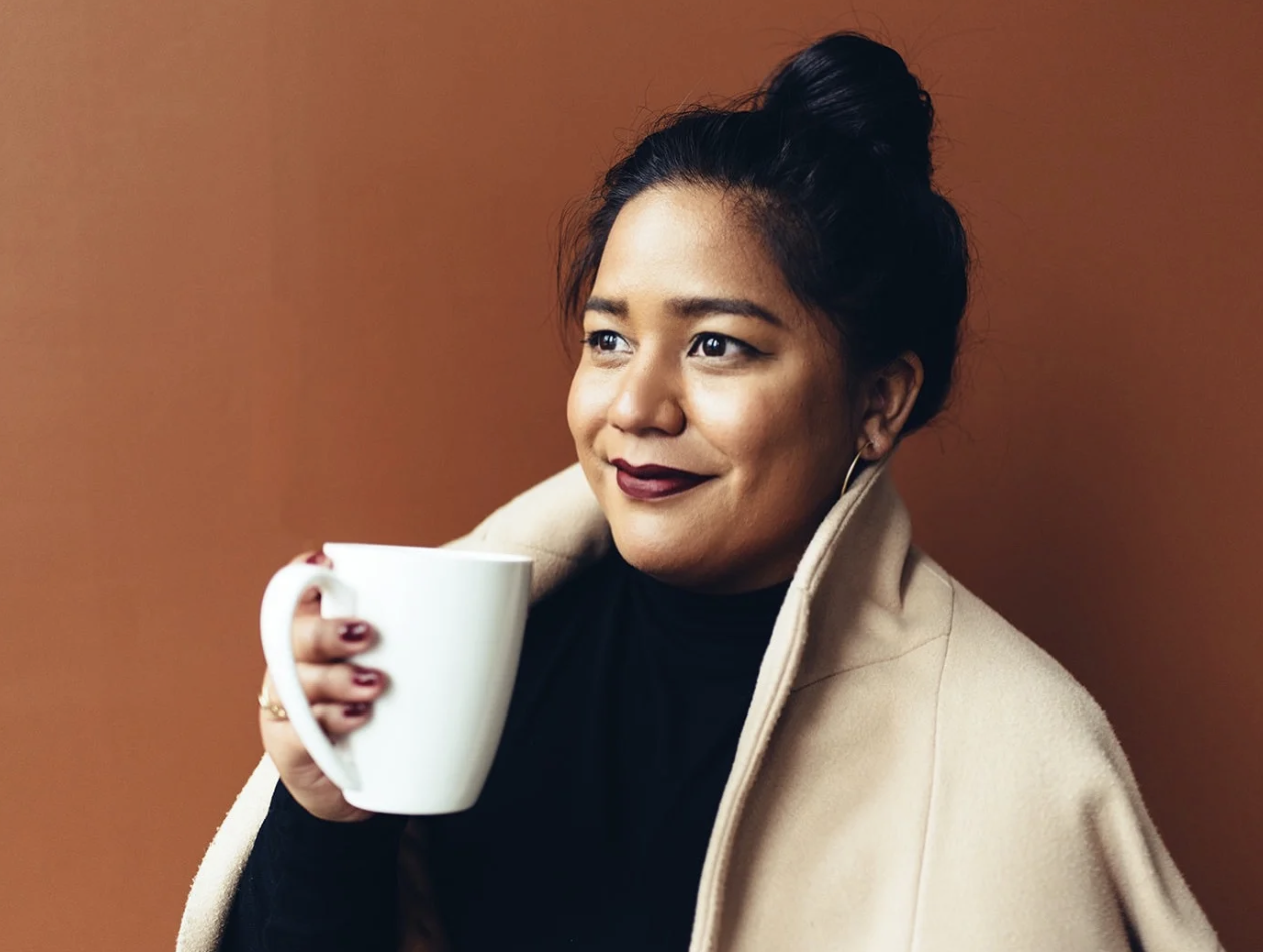 Smiling pasifika woman holding a mug, looking off into the distance to the right