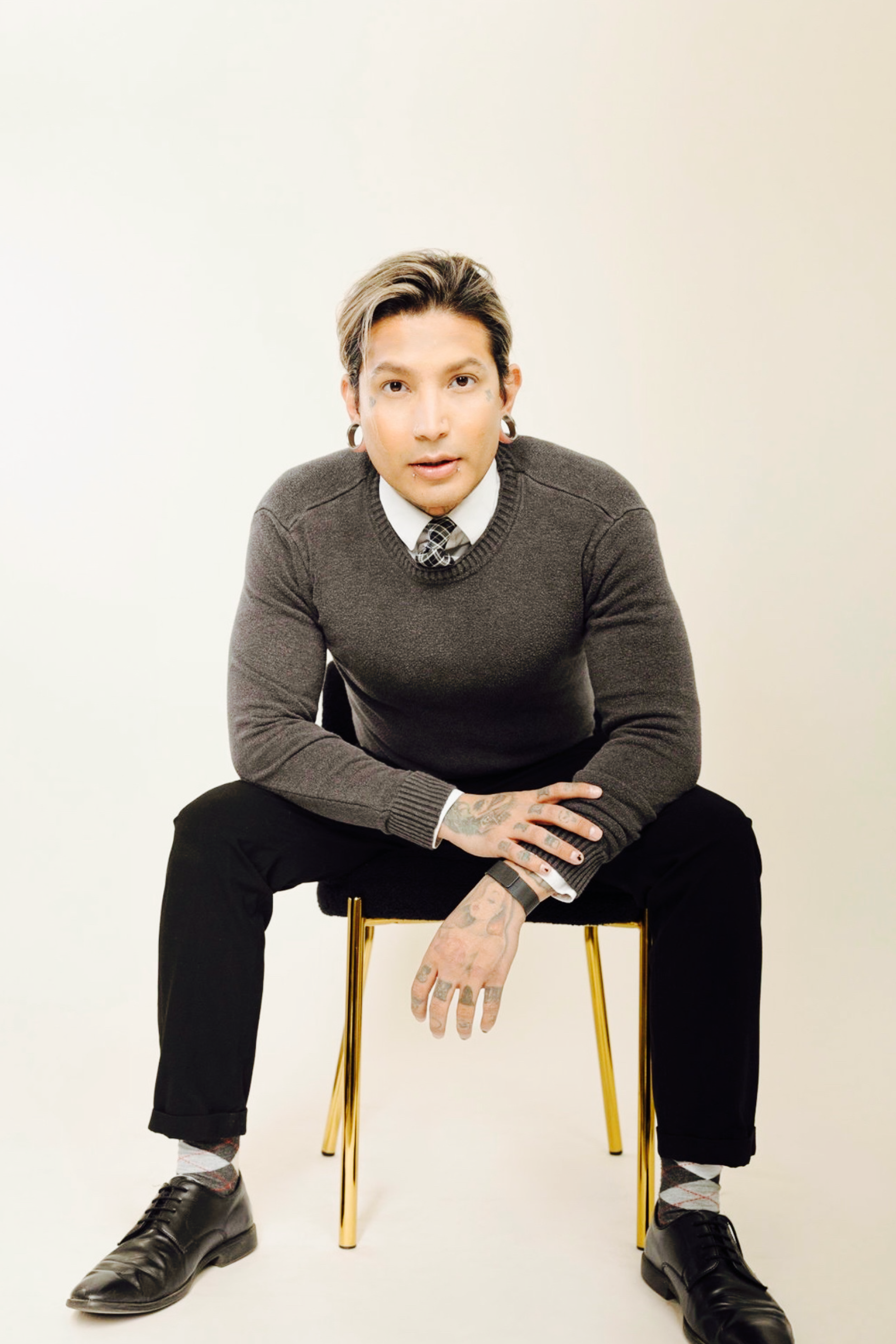 Meet Toni Ponce, Operations and Human Resource Specialist at Exclusive Business Concierge. Image of Toni wearing a gray sweater, white shirt, and black pants, sitting on a gold-legged chair against a plain white background.