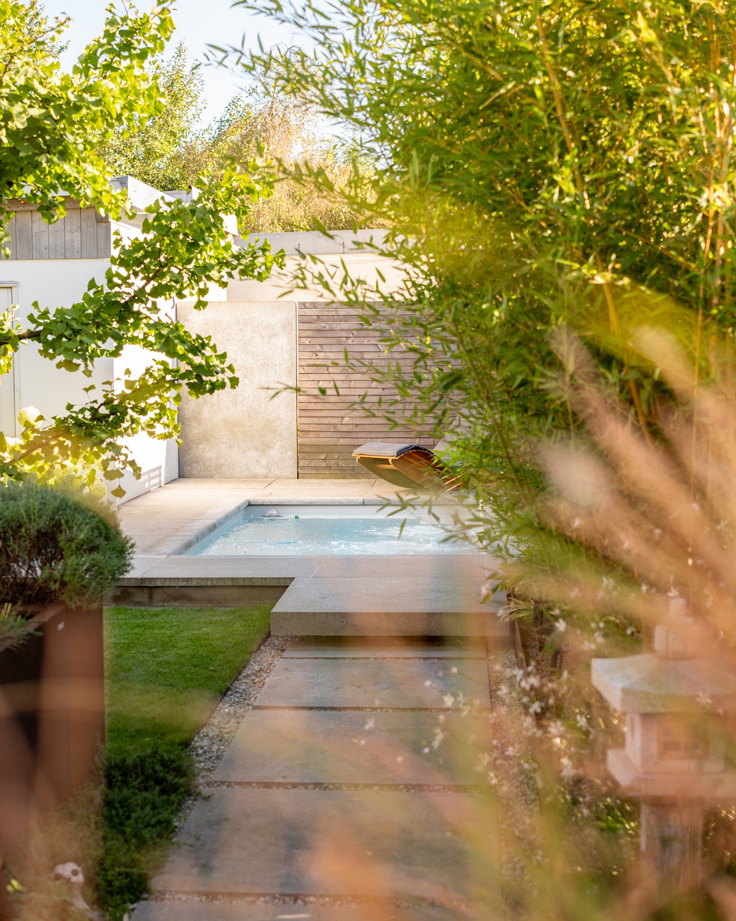 Ein Garten, der Ruhe atmet und gleichzeitig Kraft schenkt: Der Seaside Pool, umrahmt von den markanten Schellevis-Strukturbetonplatten, wird zum Herzst&uuml;ck dieser Oase. Das klare Wasser, eingebettet in viel Gr&uuml;n, l&auml;dt ein zum Verweilen,