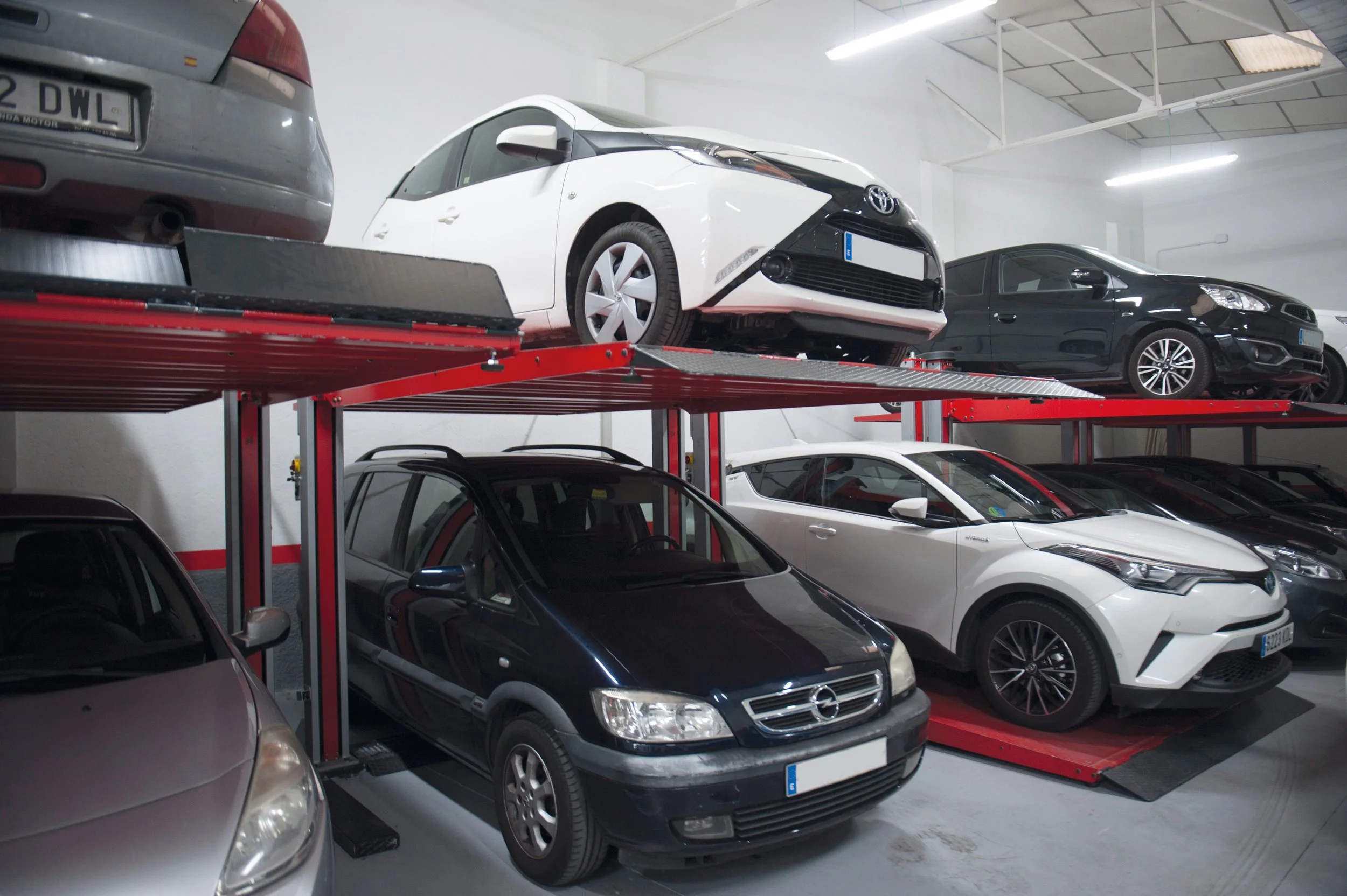 Véhicules stockés sur un système de stationnement en rotation dans un garage, avec des voitures à deux niveaux, dont des voitures blanches, noires et grises.