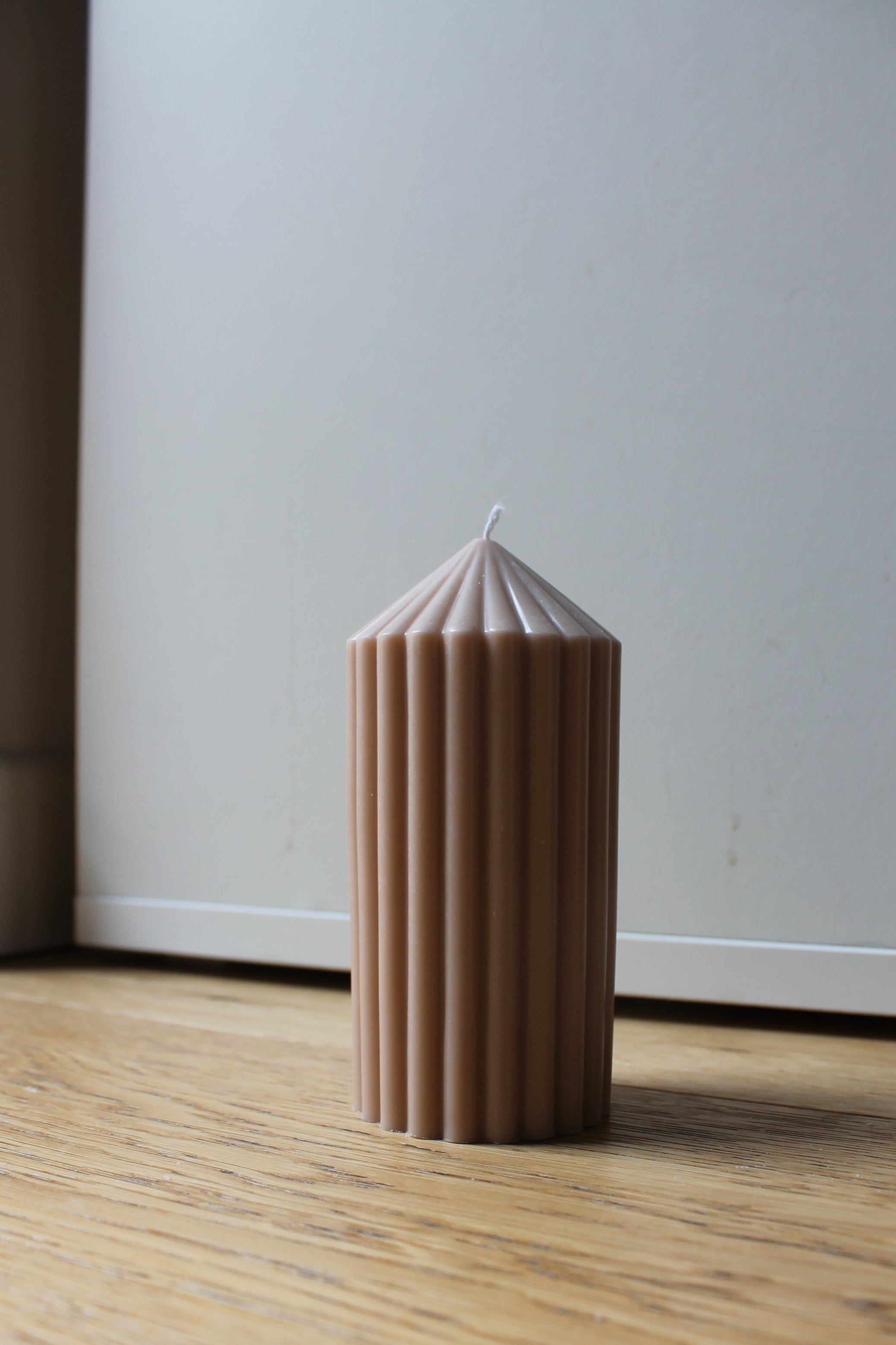 A single candle placed on a wooden table, casting a soft glow in a dimly lit room.