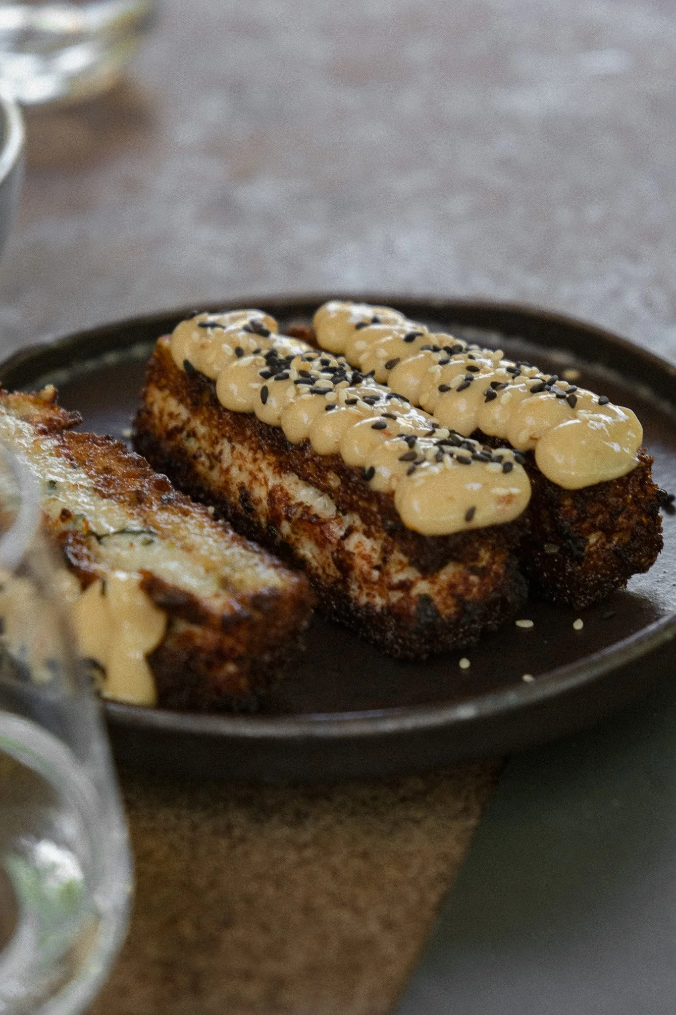 Close-up of a baked snack topped with white cream, black sesame seeds, and white sesame seeds on a black plate.