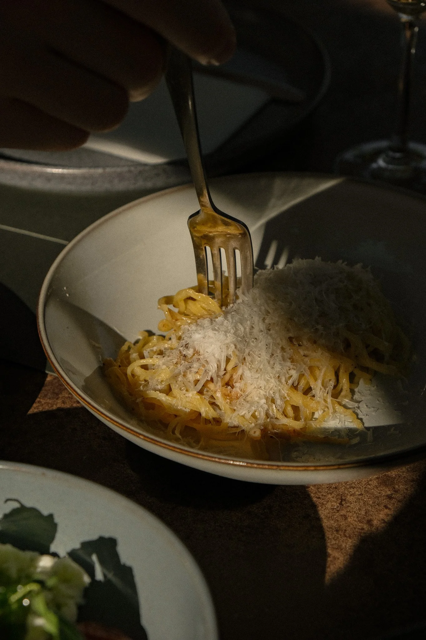 Close-up of a plate of spaghetti with grated cheese on top, with a fork twirling some noodles, set on a dark surface.