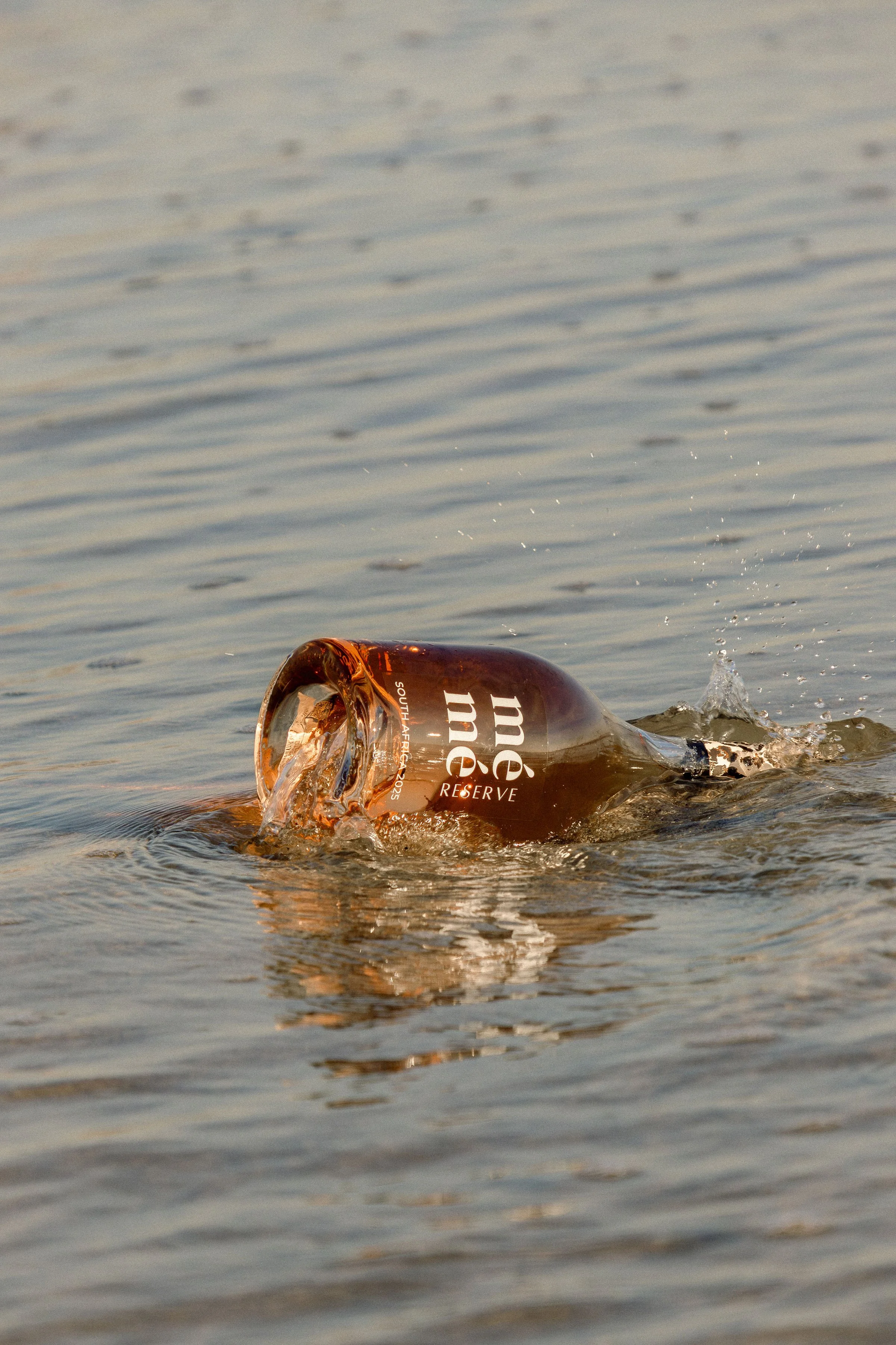 A beer bottle partially submerged in water with noticeable ripples and splashes around it.