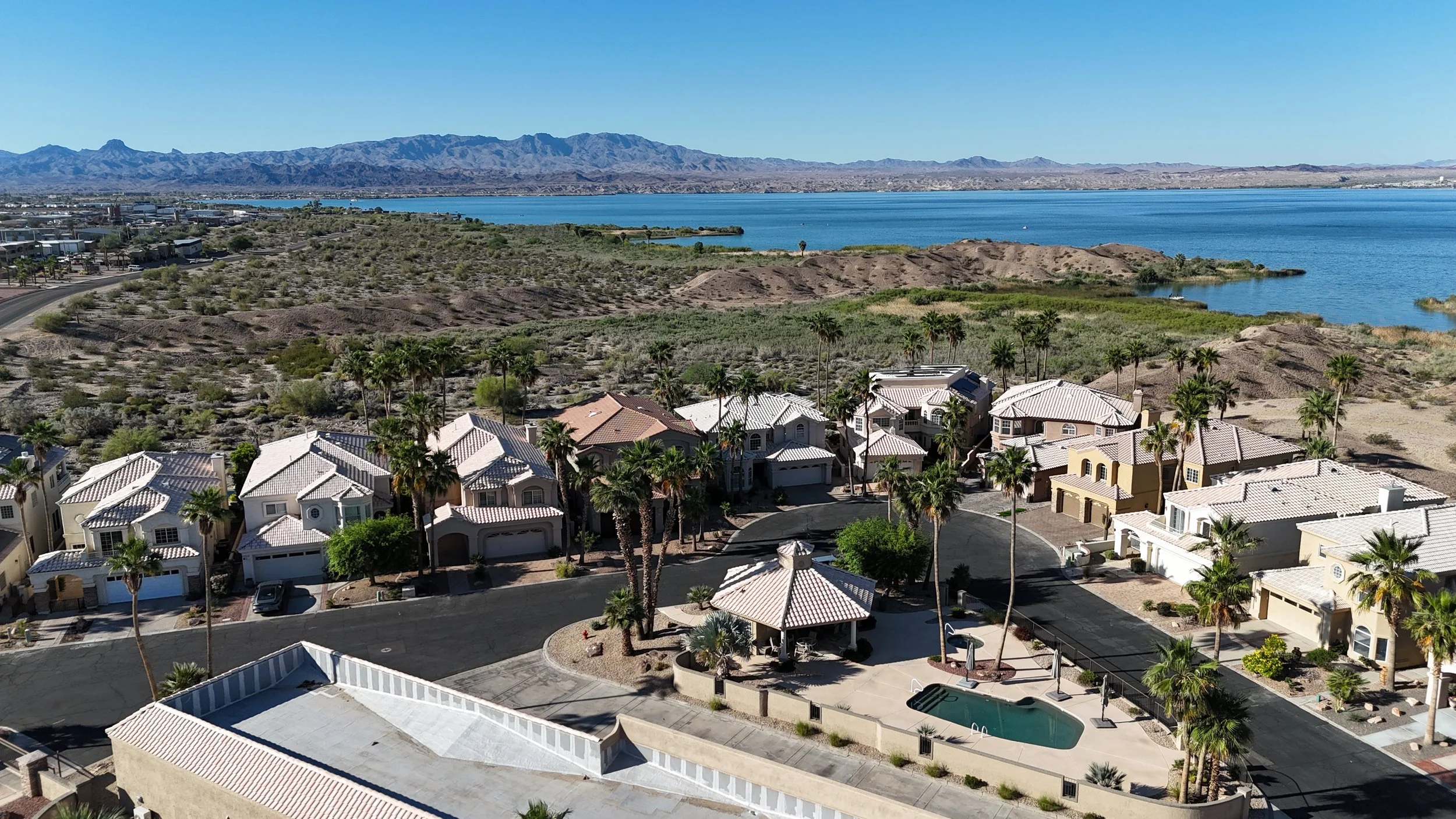 Aerial view of a marina with boats docked on a body of water, neighboring residential buildings, and a desert landscape in the background.