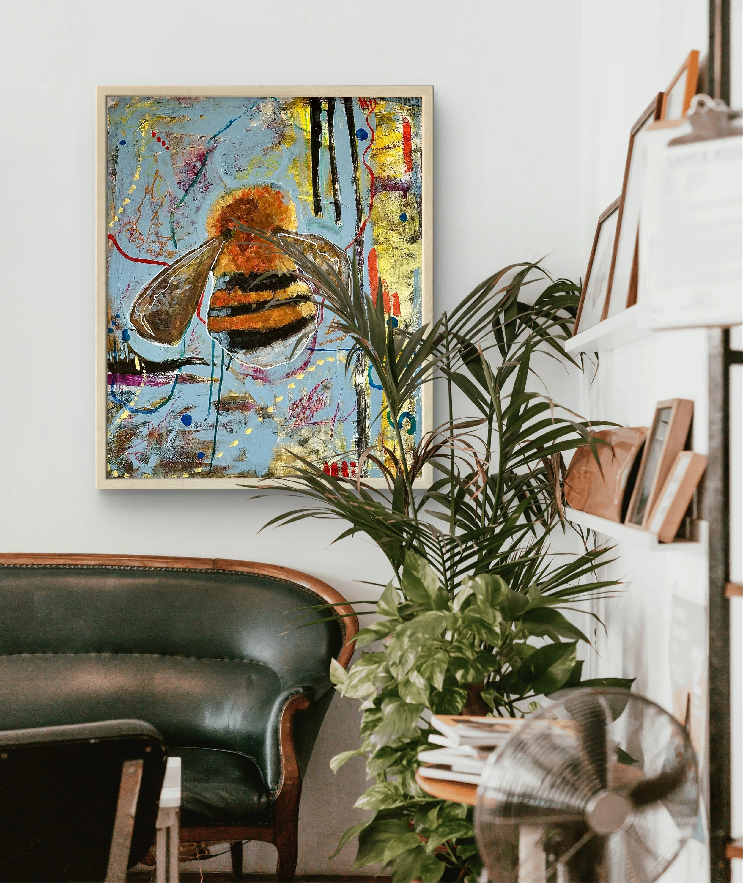 Interior of a room with a colorful abstract painting of a bee on a light-colored wall, an antique green leather chair, a tall indoor plant, and wall shelves with books and artwork.