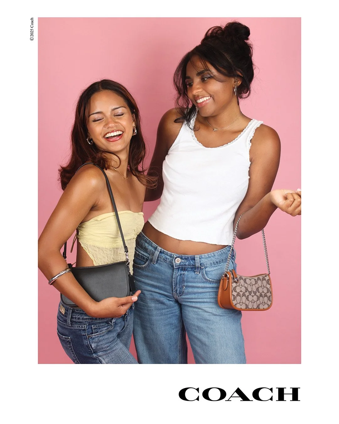 Two women smiling and laughing against a pink background, wearing casual outfits, with handbags.