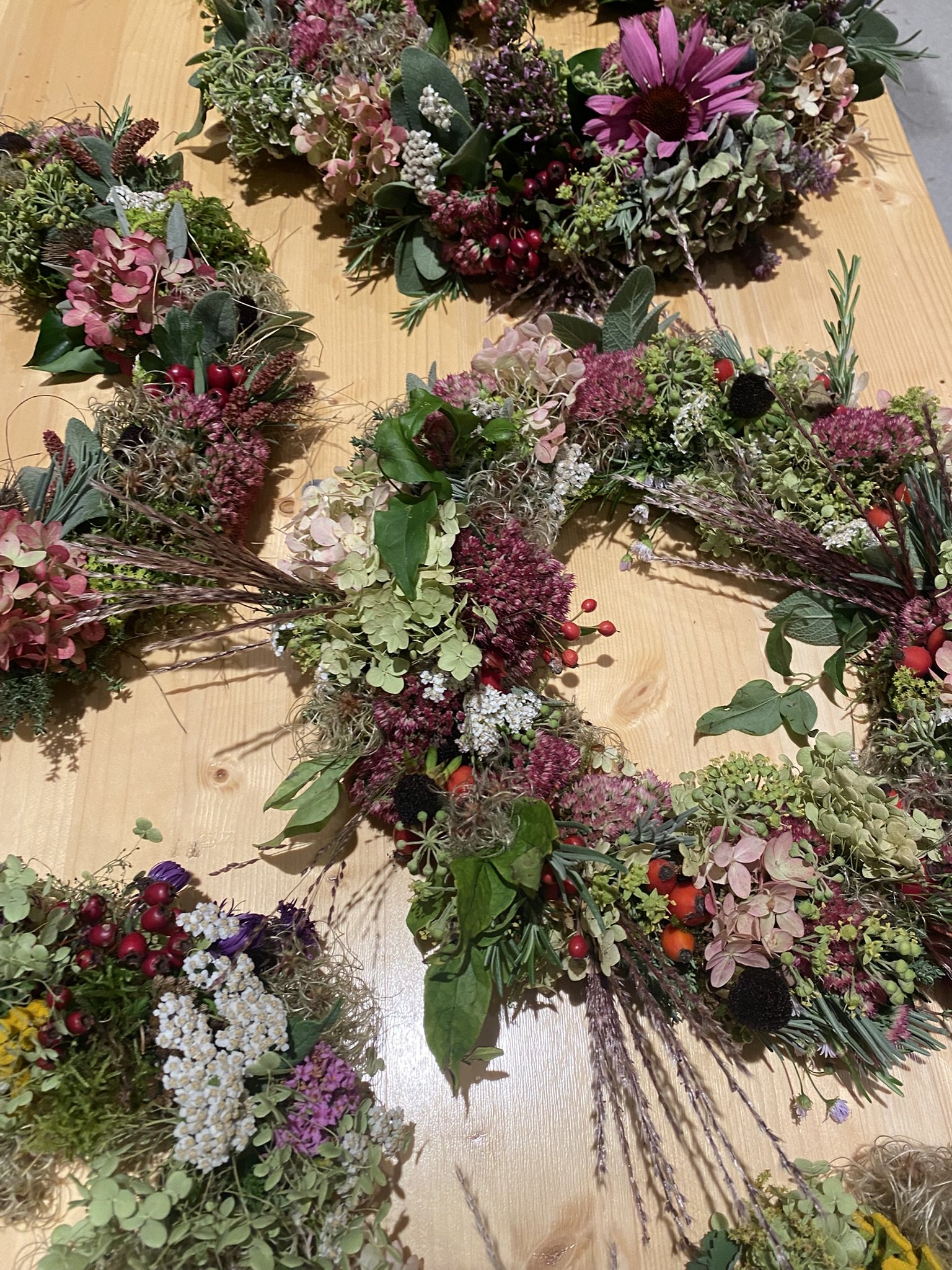 Blumenkränze mit verschiedenen pinken, weißen, grünen und violetten Blumen und Blättern auf einer Holztischoberfläche.