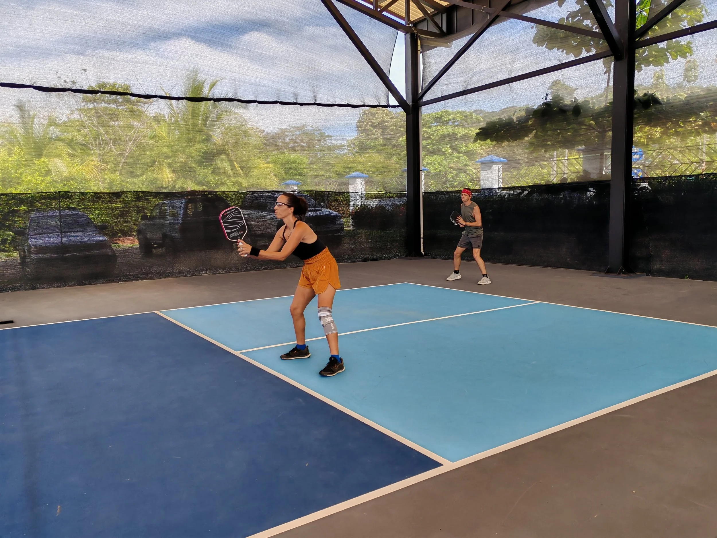 A couple playing pickleball, in southern Costa Rica, getting ready to hit a ball on a covered court.