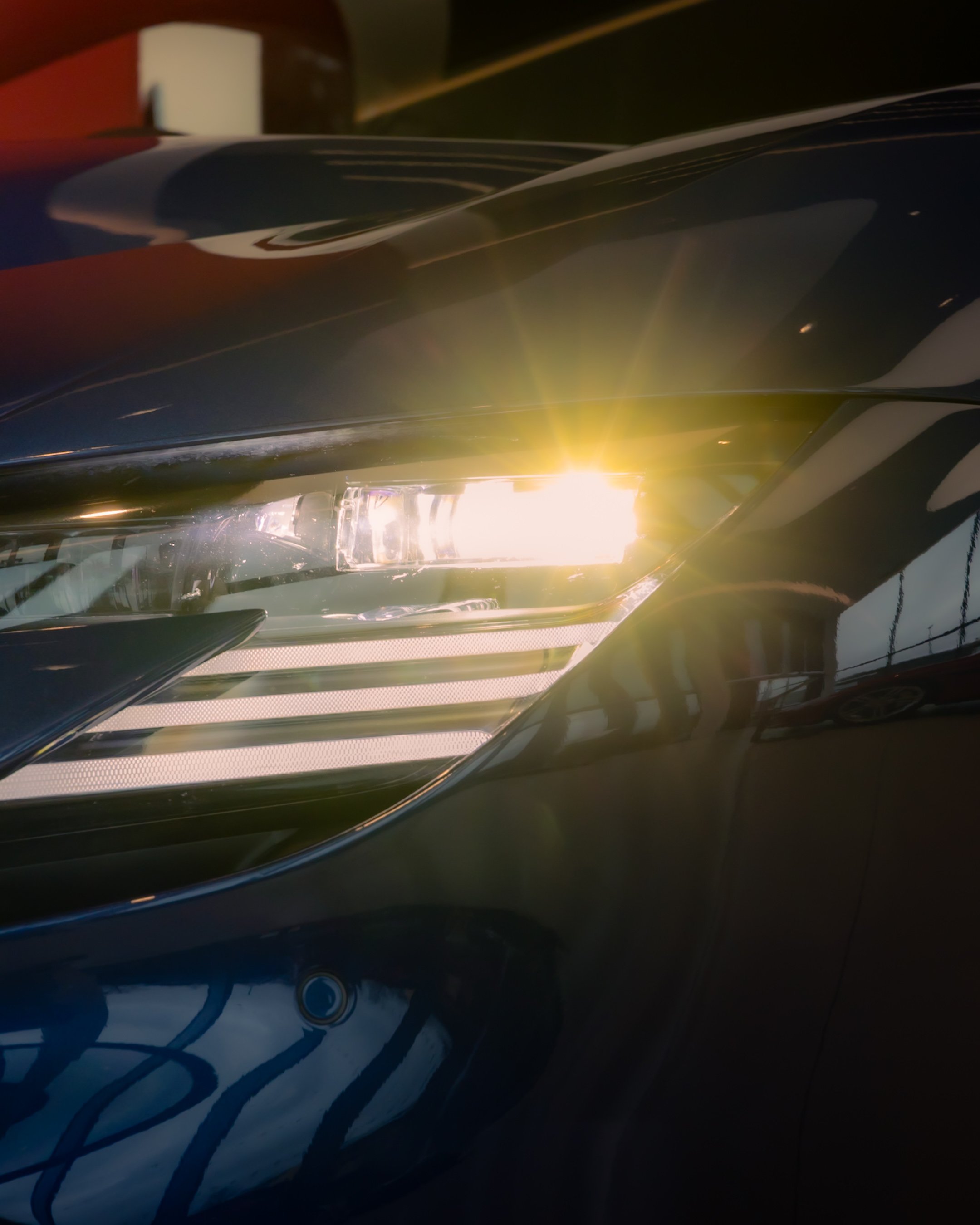 Close-up of a car headlight with a bright light shining, showing reflections on the car's surface.