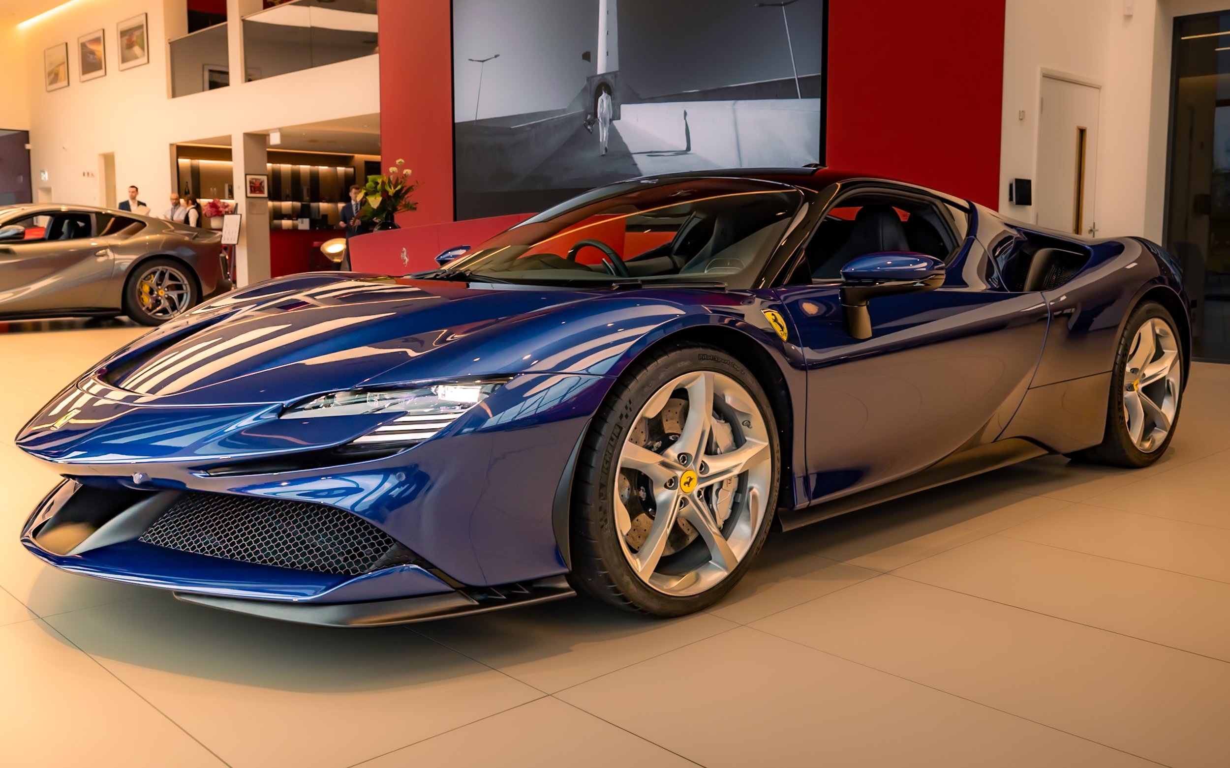Blue sports car displayed in a showroom with glass and red walls.