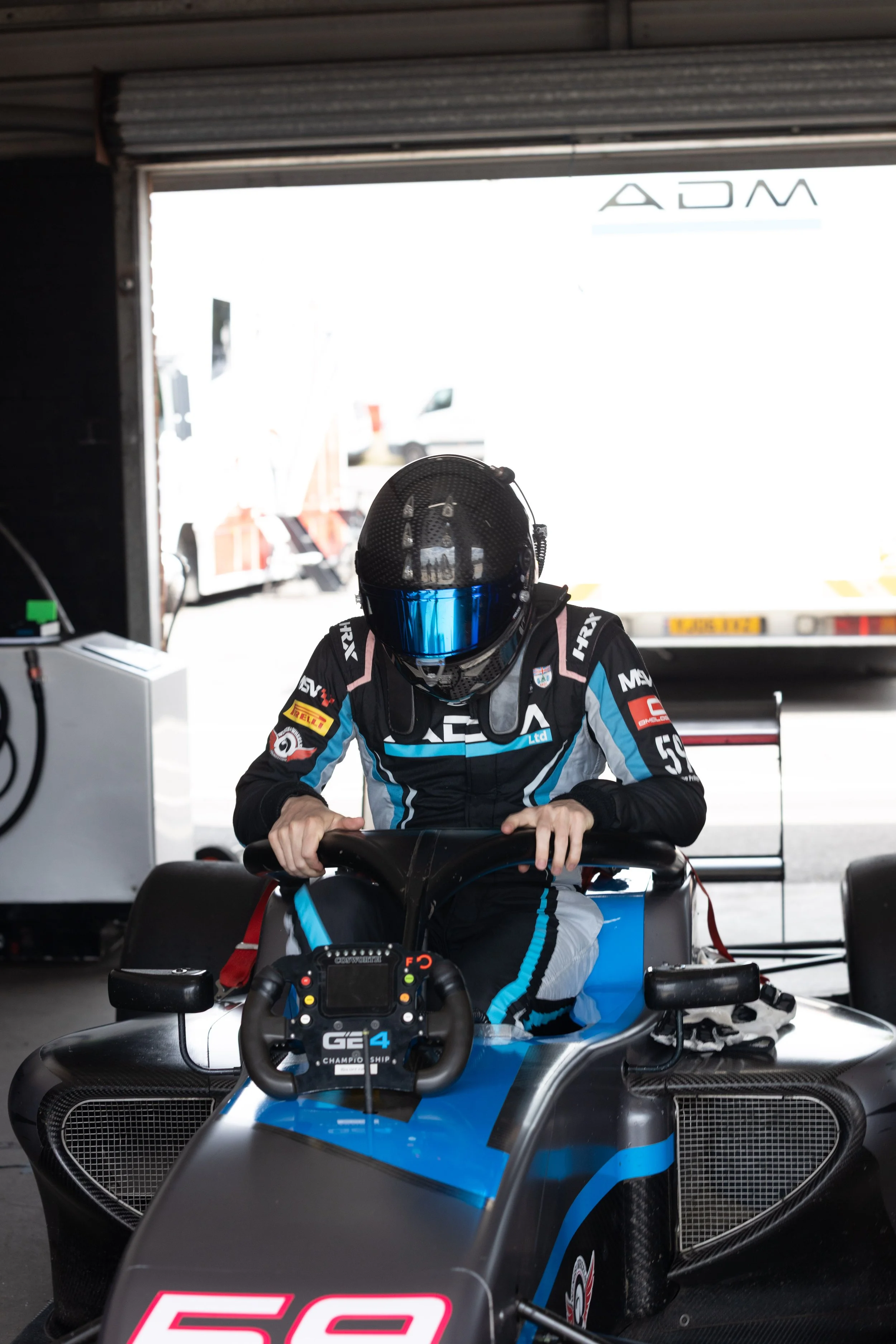 Race car driver in racing suit and helmet sitting in a race car at the garage, preparing for a race.