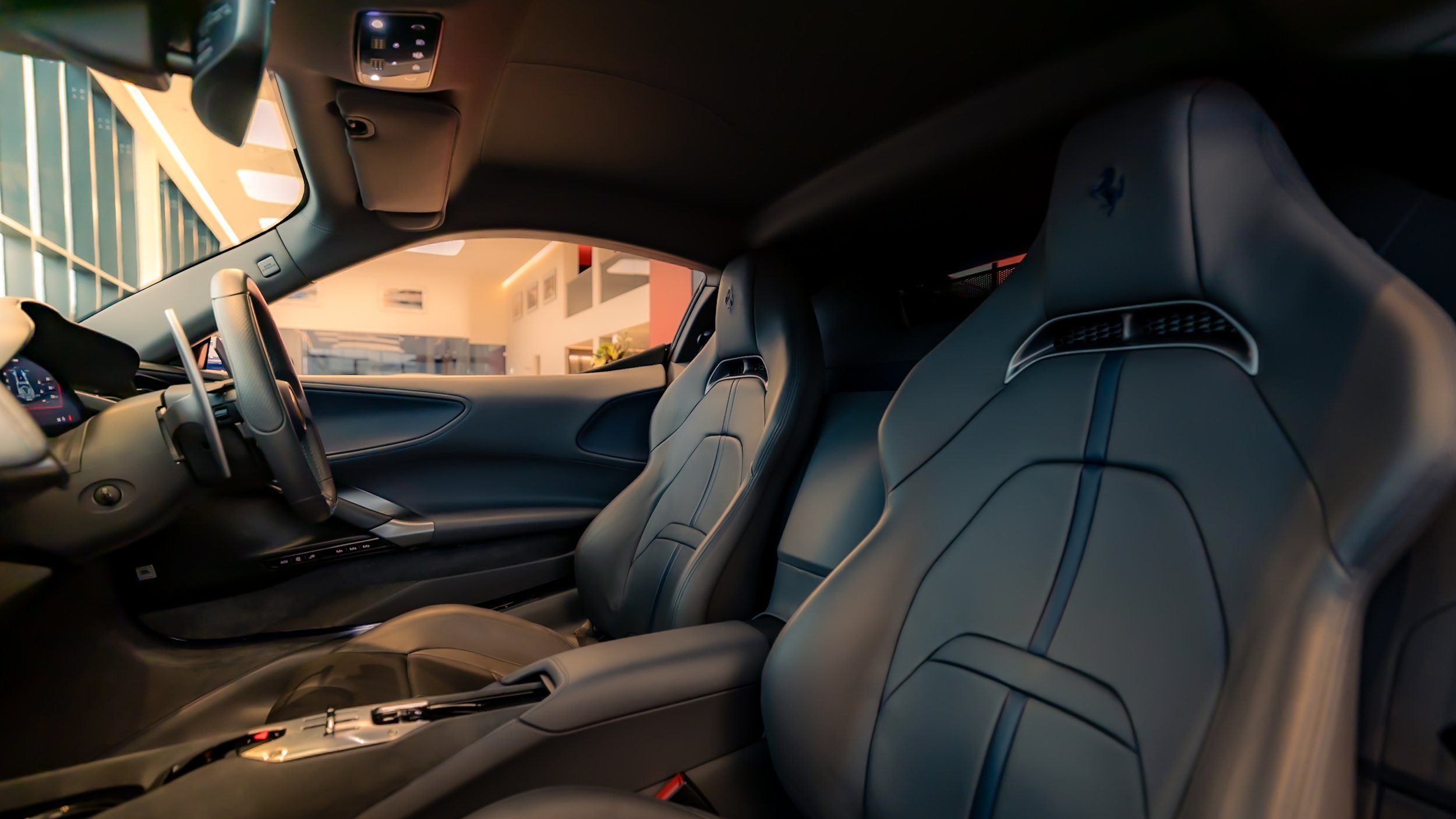 Luxury sports car interior with leather seats and dashboard, featuring a steering wheel and console controls, inside a modern showroom.
