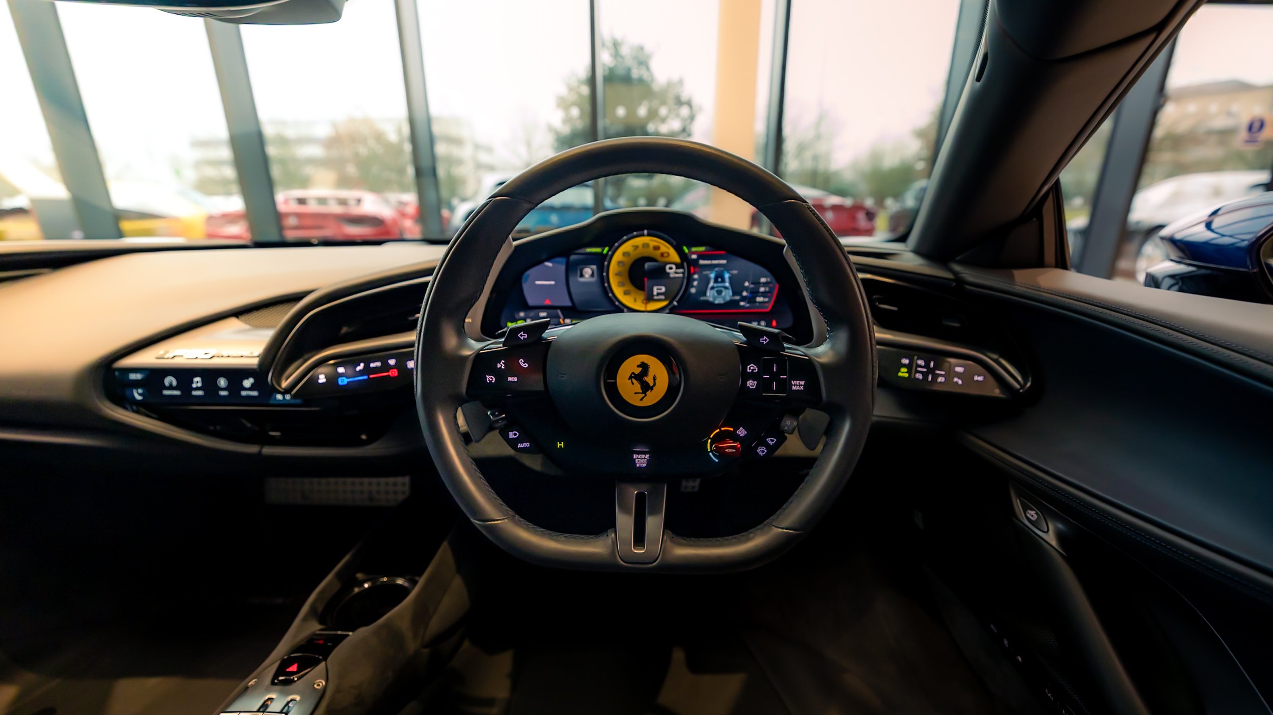 Interior of a luxury sports car focusing on the steering wheel with a logo, digital displays, and control buttons visible.