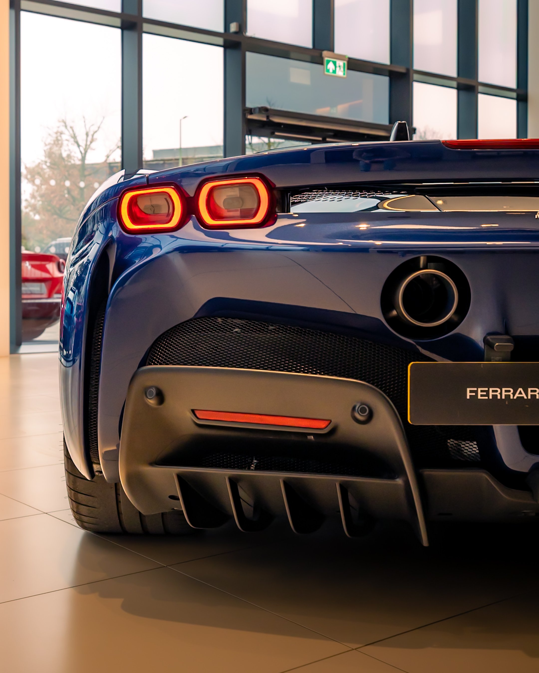 Rear view of a blue sports car with dual exhaust and red taillights, displayed in a showroom.