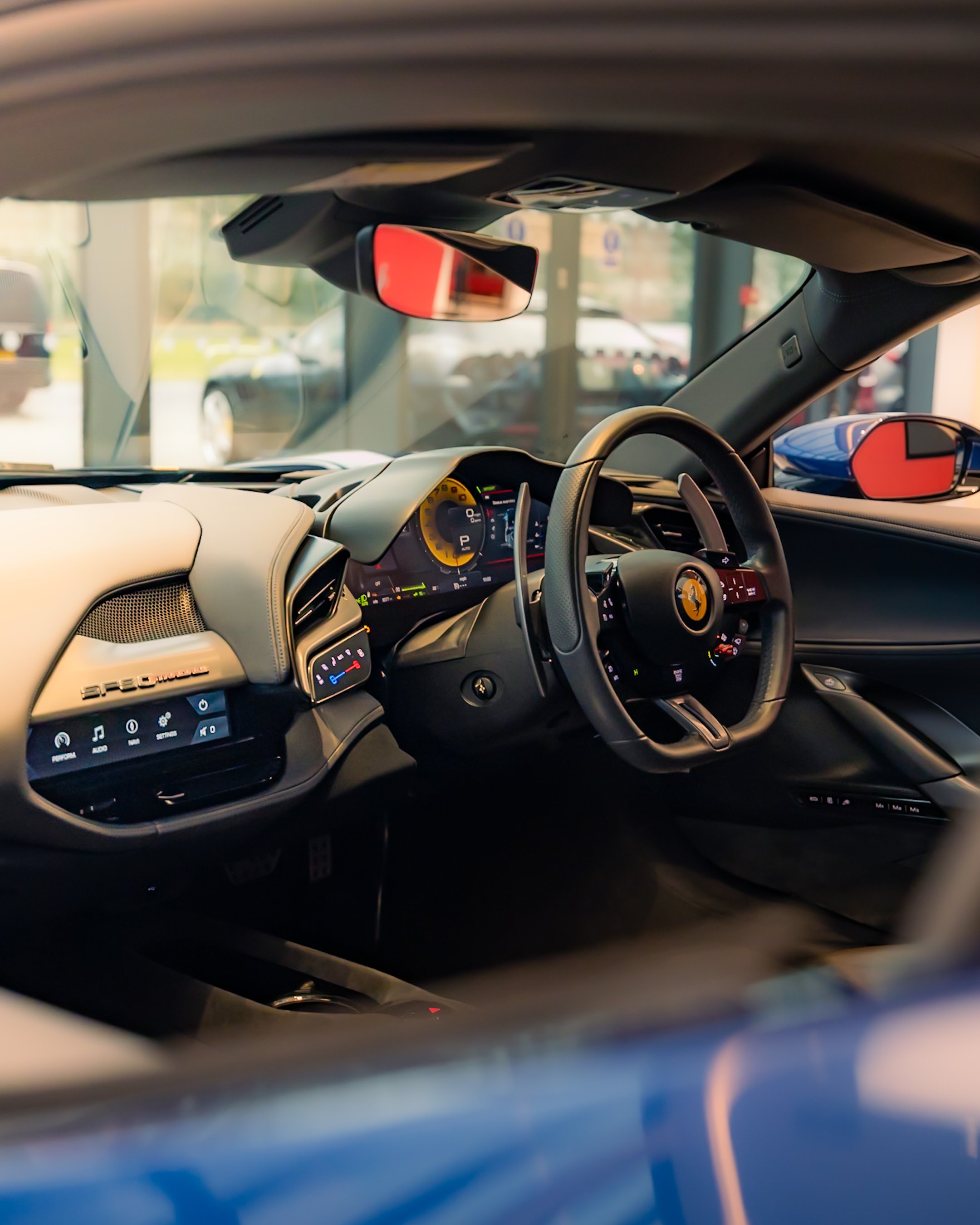 Interior of a luxury car focusing on the driver's seat and dashboard, featuring a steering wheel with a yellow emblem, digital display panels, and leather upholstery.