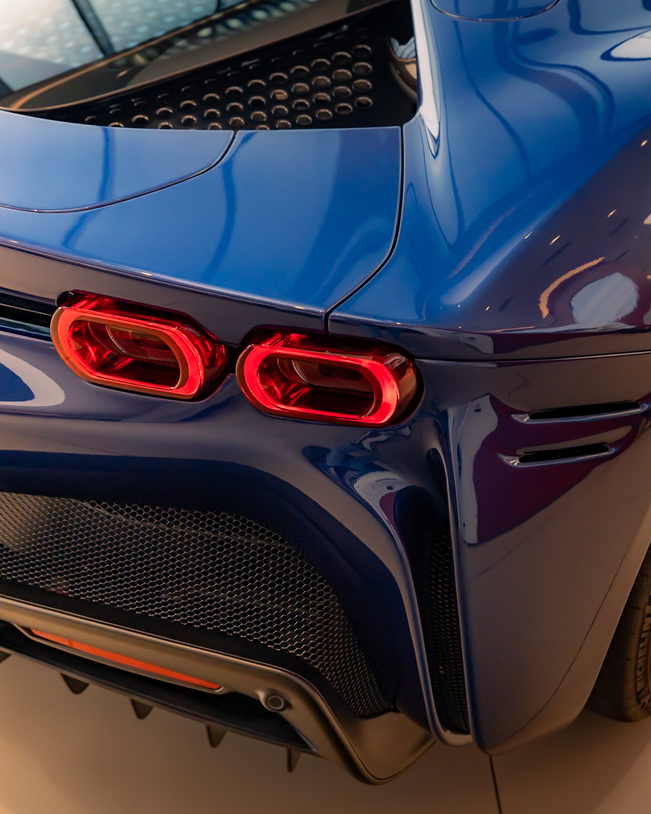 Close-up of a blue sports car's rear, showing red taillights and aerodynamic design.